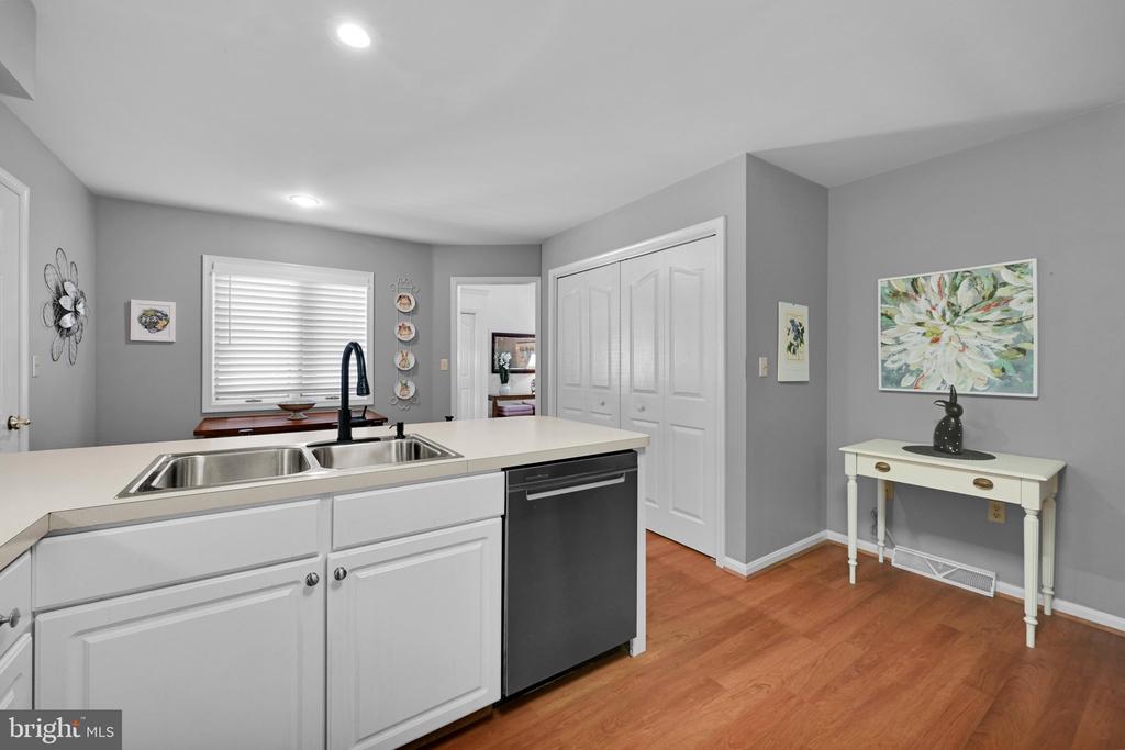 Kitchen with white cabinets, an island sink, black dishwasher, gray walls, and warm wood flooring.