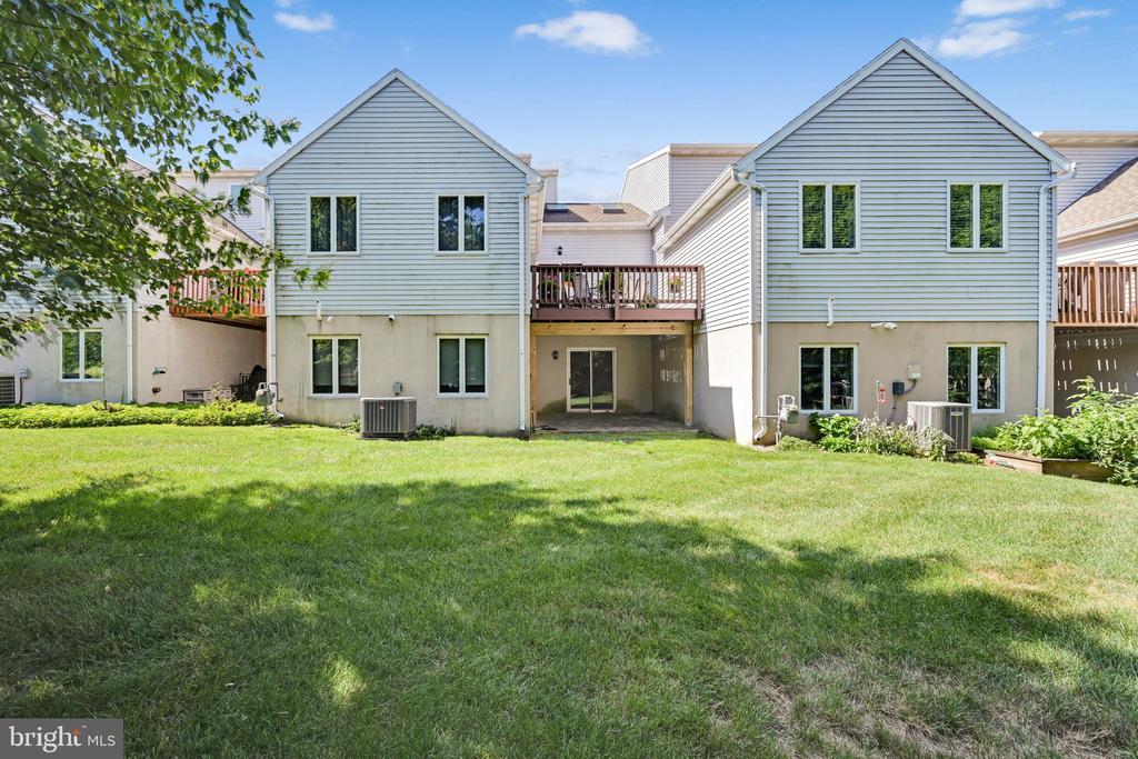 Rear of the home with pale blue siding, wooden decks, a covered patio, and a broad grassy yard.