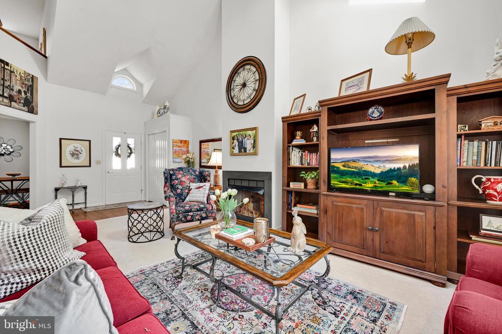 Vaulted living room with a fireplace, wooden built-in bookshelves, red sofas, and a floral armchair.