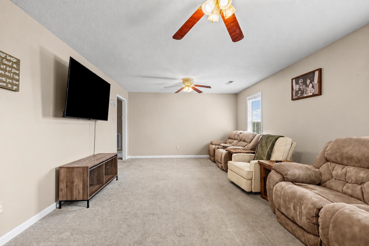 Living room with tan recliners, wall-mounted TV, beige carpet, and two ceiling fans.