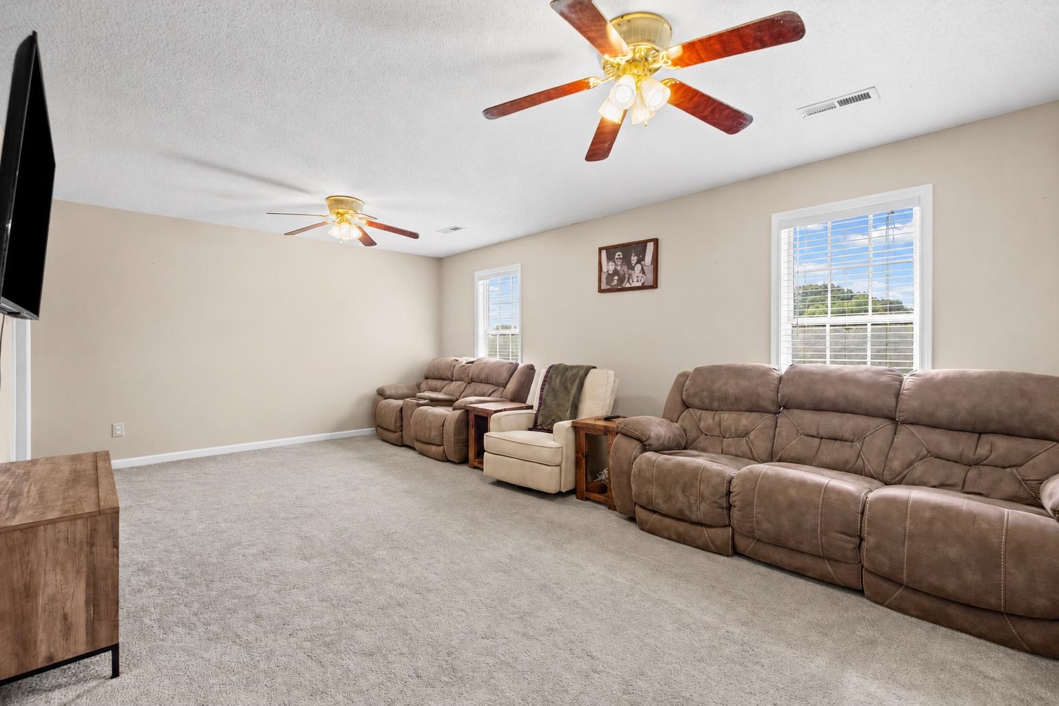 Living room with brown leather reclining sofas, beige carpet, and two ceiling fans.