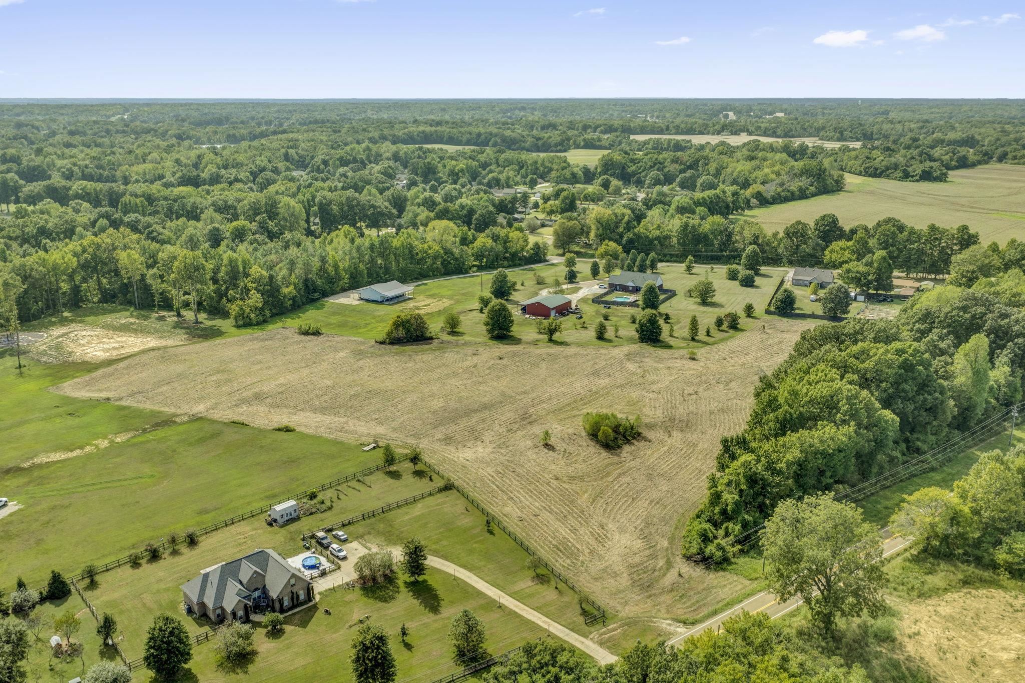 Aerial view of rural acreage with open fields, scattered homes, and surrounding woodland.