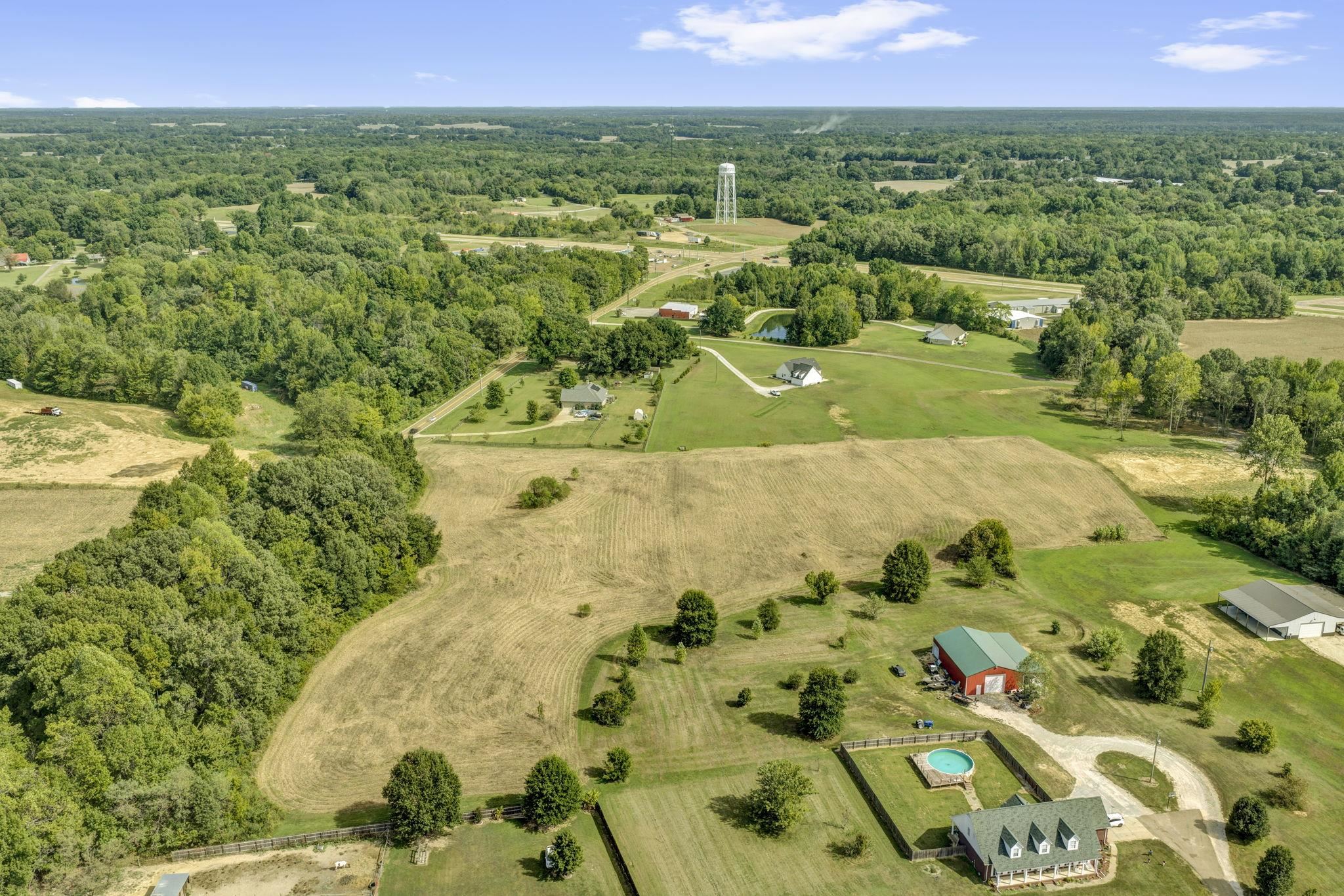 Aerial view of rural parcels with cleared fields, surrounding woods, and scattered homes.