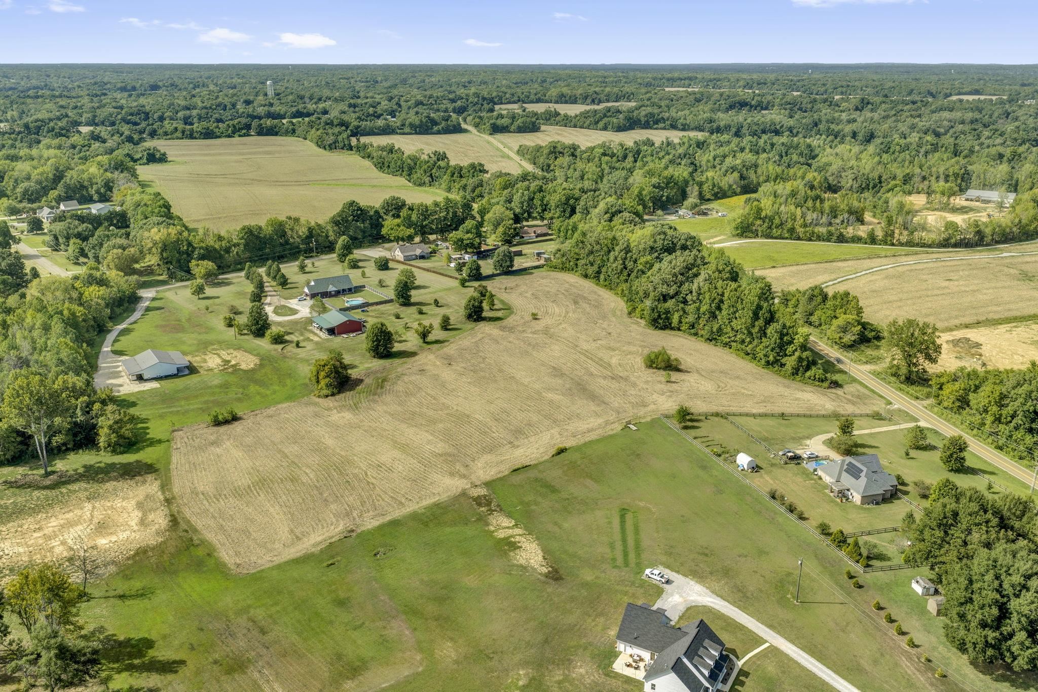 Aerial view of cleared rural fields bordered by woods, with scattered homes and roads nearby.