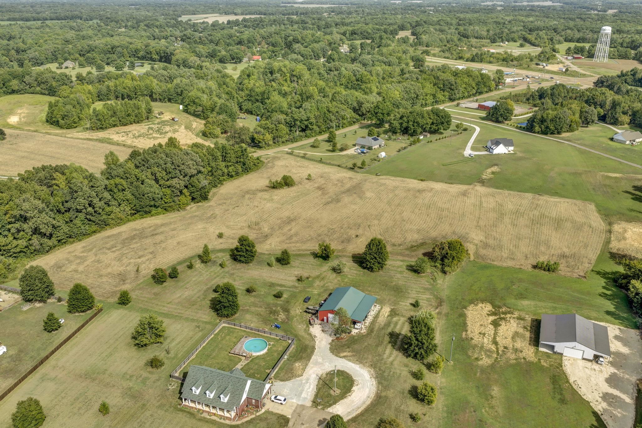 Aerial view of rural lots with broad fields, surrounding trees, and scattered homes and outbuildings.