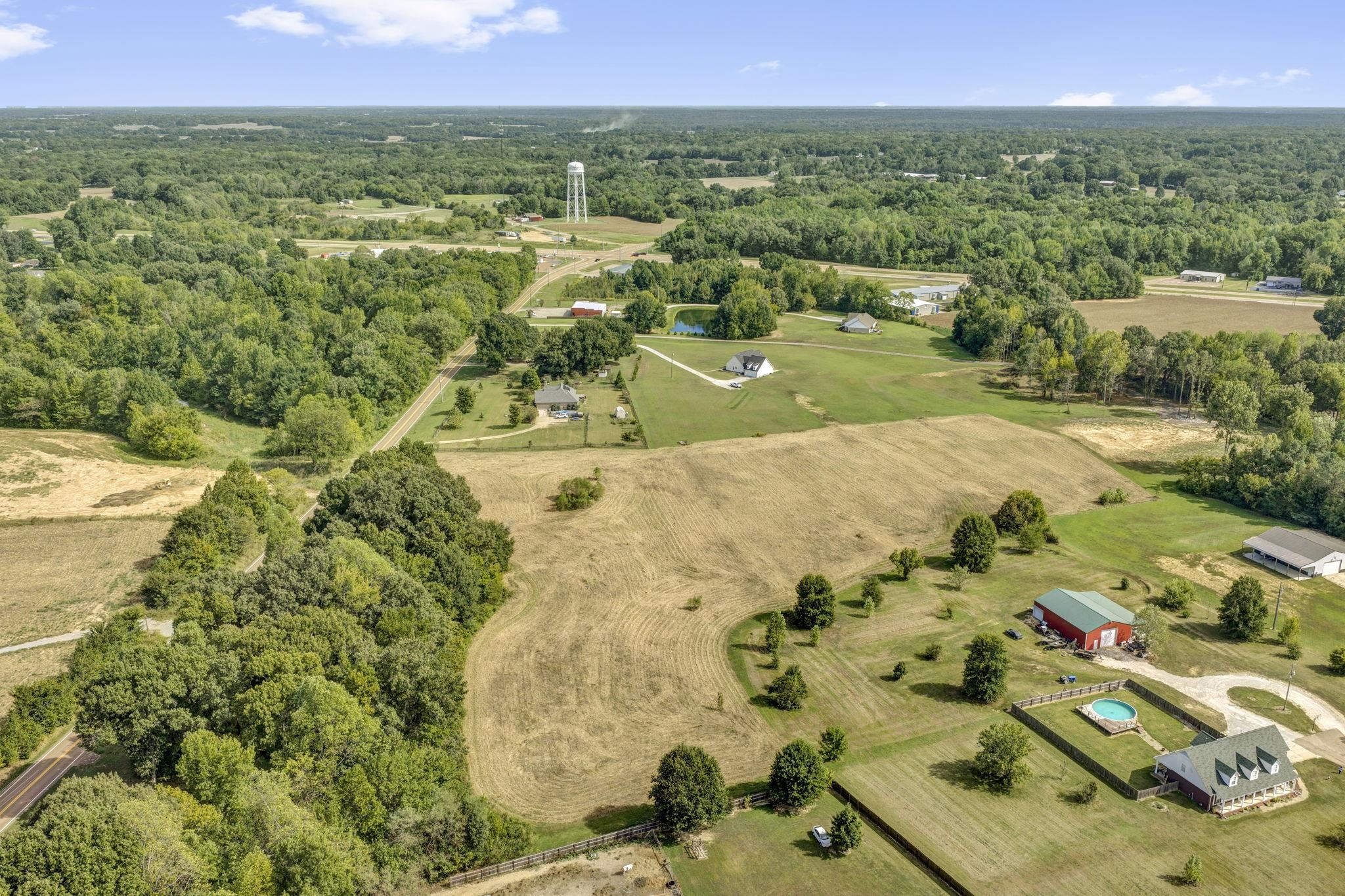 Aerial view of rural fields and woods, with scattered homes and a distant water tower.