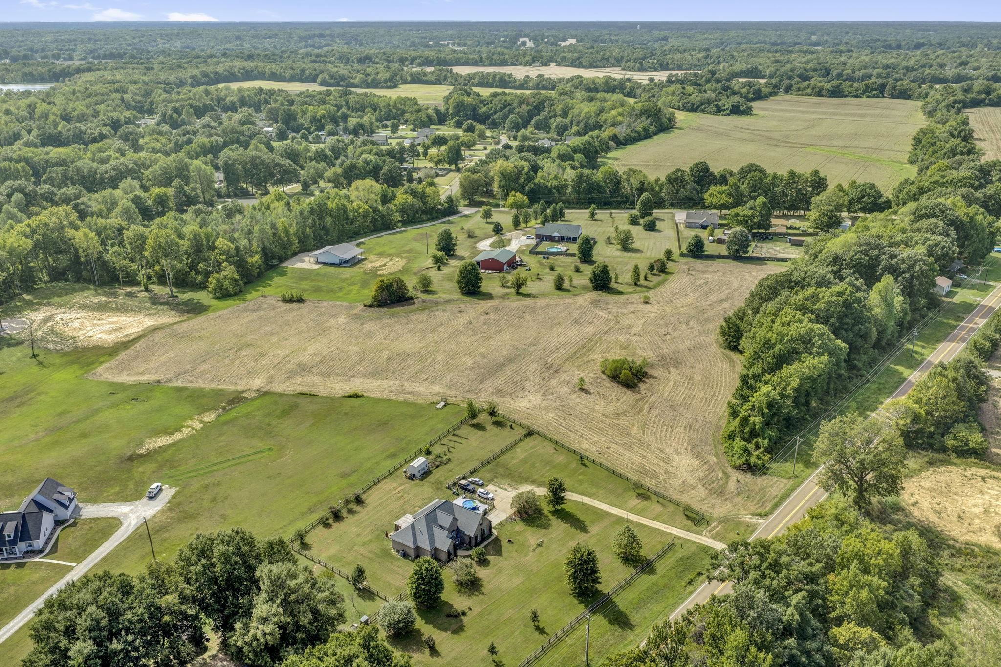 Aerial view of a plowed field bordered by pasture, trees, nearby homes, and a paved road.