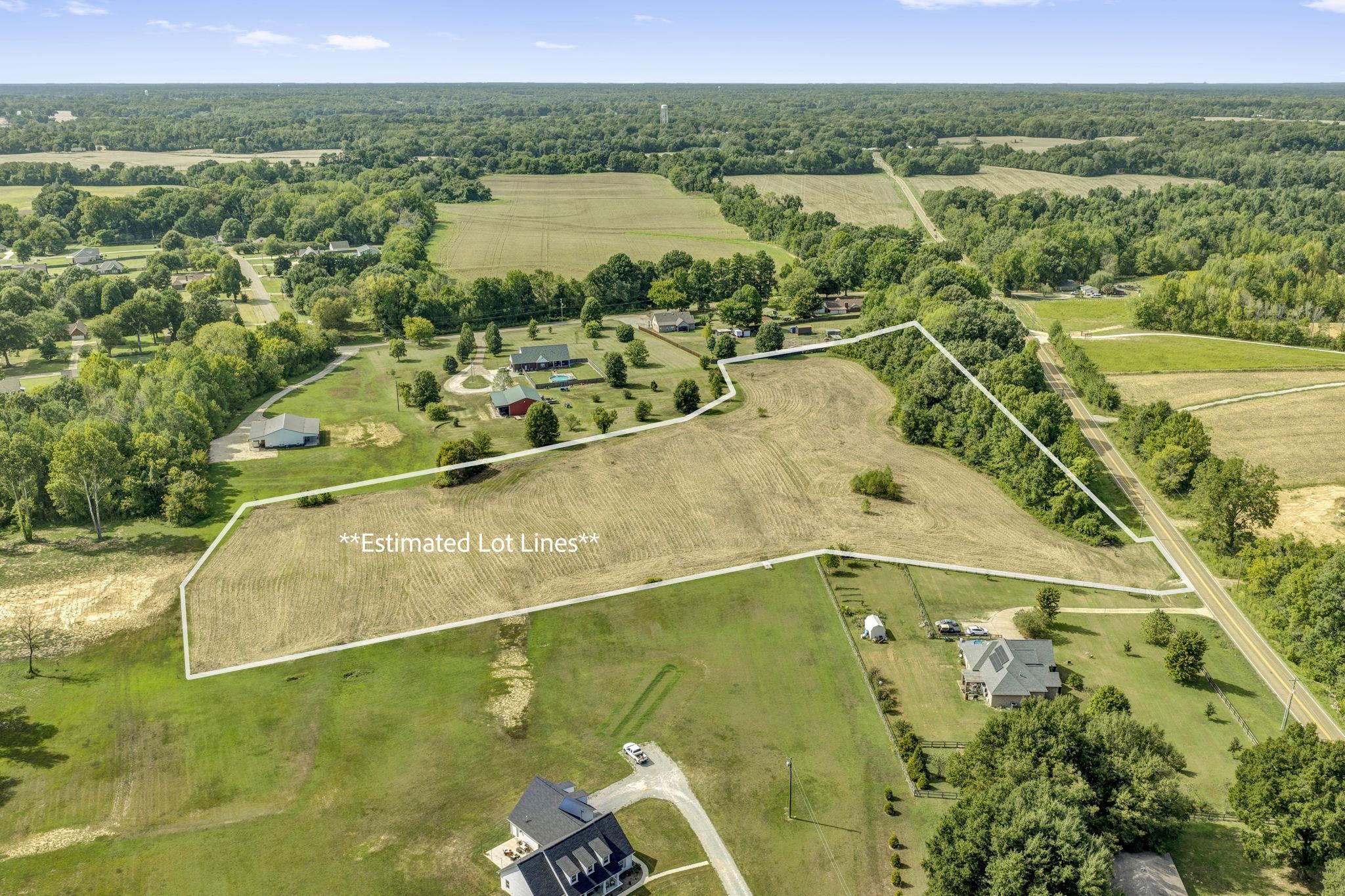 Aerial view of a cleared parcel outlined as estimated lot lines, beside a road and neighboring homes.