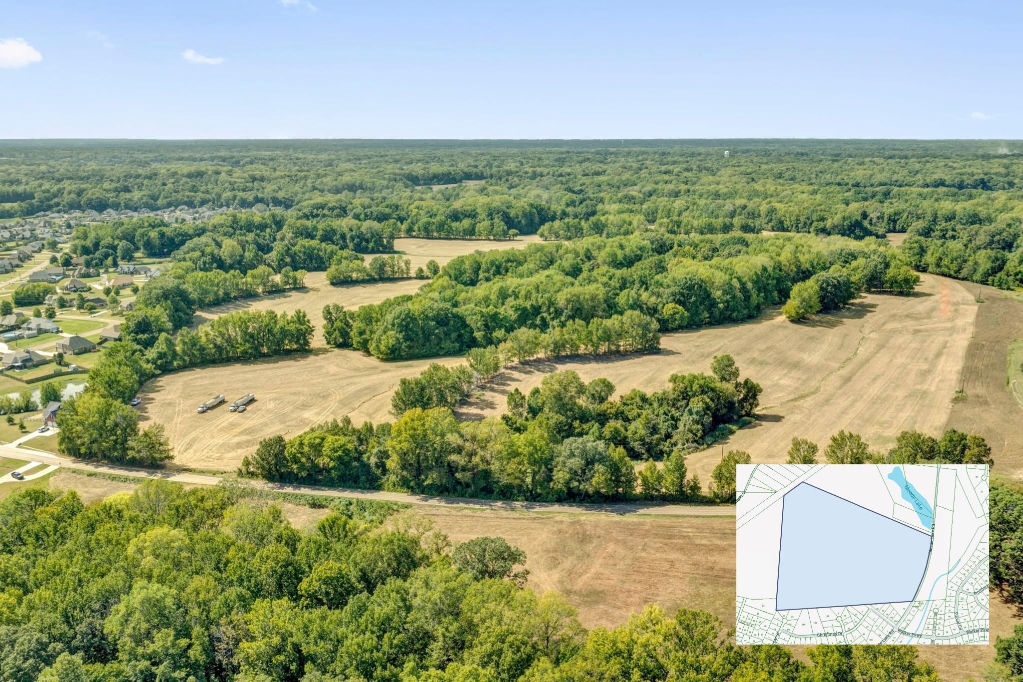 Aerial view of cleared vacant land bordered by trees, with a parcel map inset.