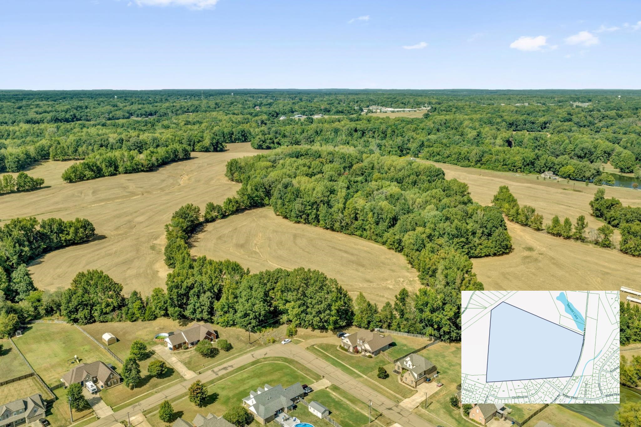 Aerial view of a large wooded and cleared parcel beside a neighborhood, with an outlined parcel map inset.