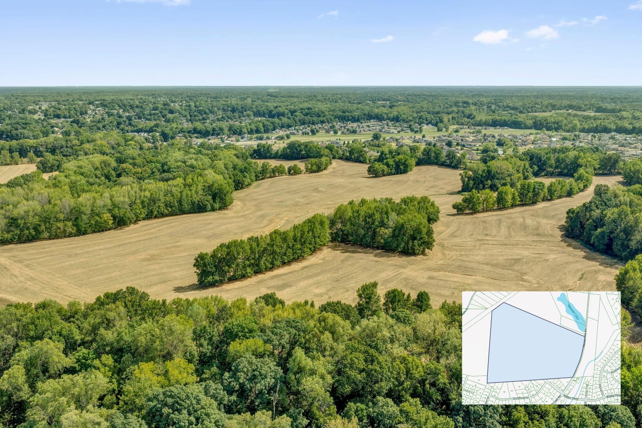 Aerial view of open fields surrounded by woods, with a parcel map inset and homes in the distance.
