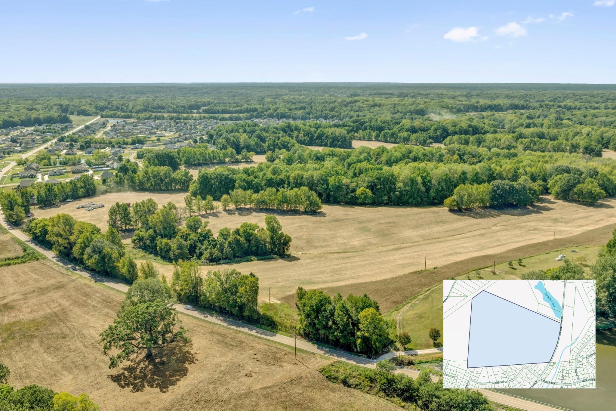 Aerial view of wooded open acreage beside a neighborhood, with a parcel map inset.