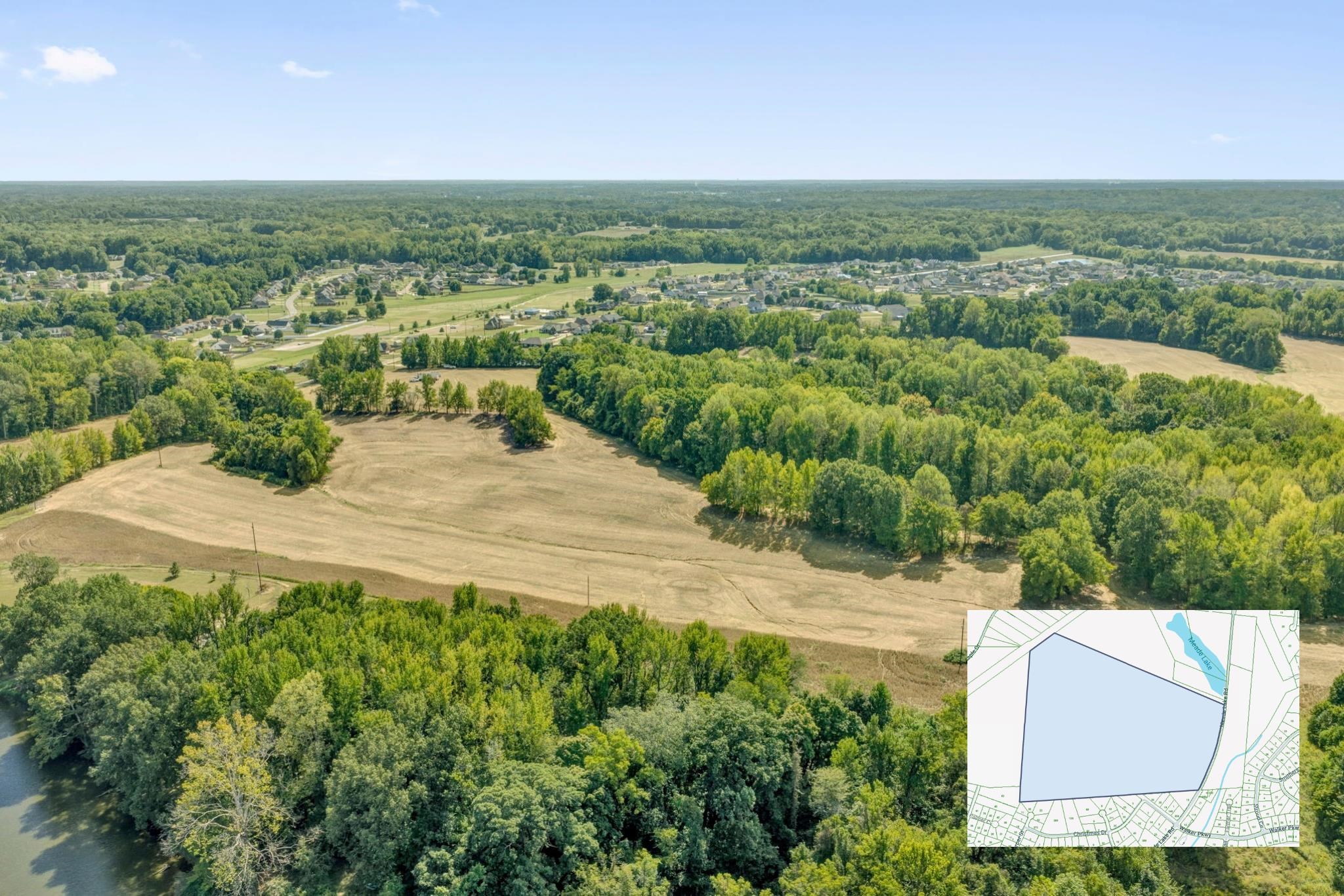 Aerial view of open fields and wooded land, with a parcel map inset and homes in the distance.