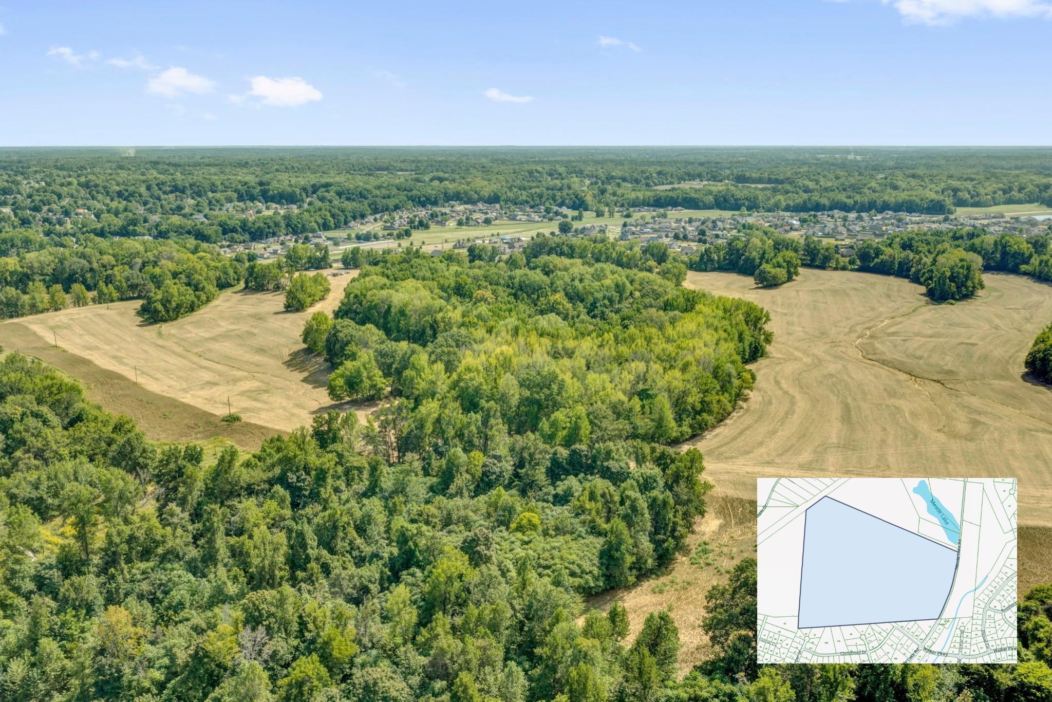 Aerial view of wooded acreage and open fields, with a parcel map inset and homes in the distance.