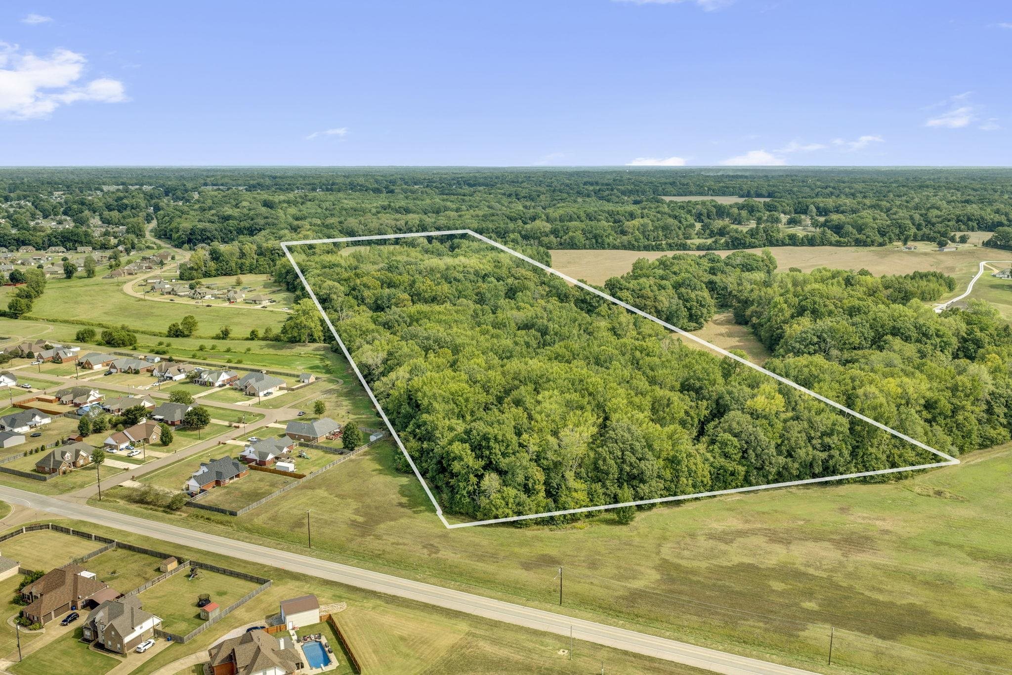 Aerial view of a wooded parcel outlined in white beside a road and neighborhood.