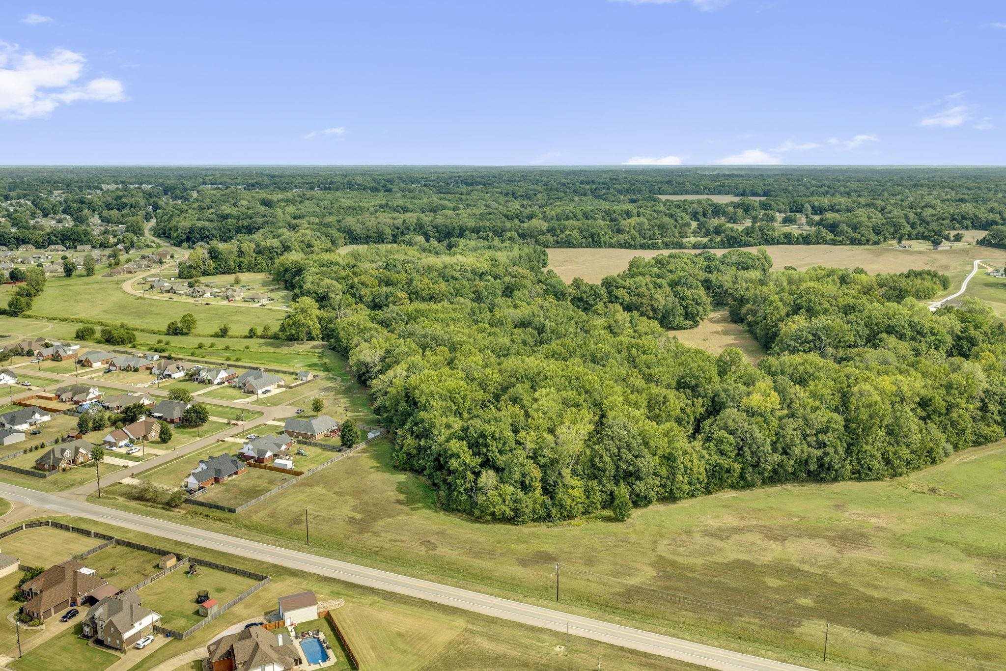 Aerial view of a wooded property beside a road and neighborhood.