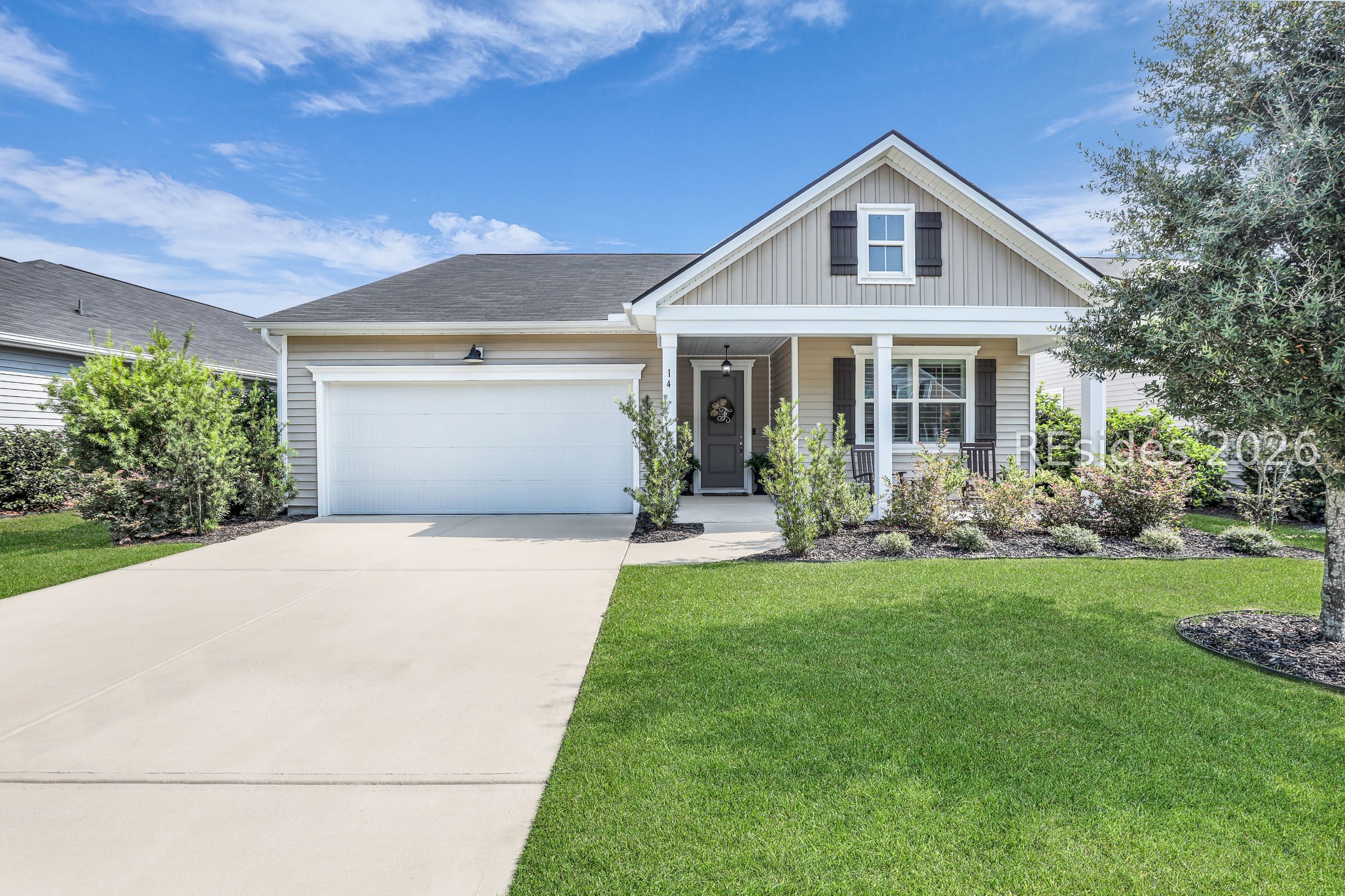 Light gray house with a front porch, attached garage, and landscaped lawn.