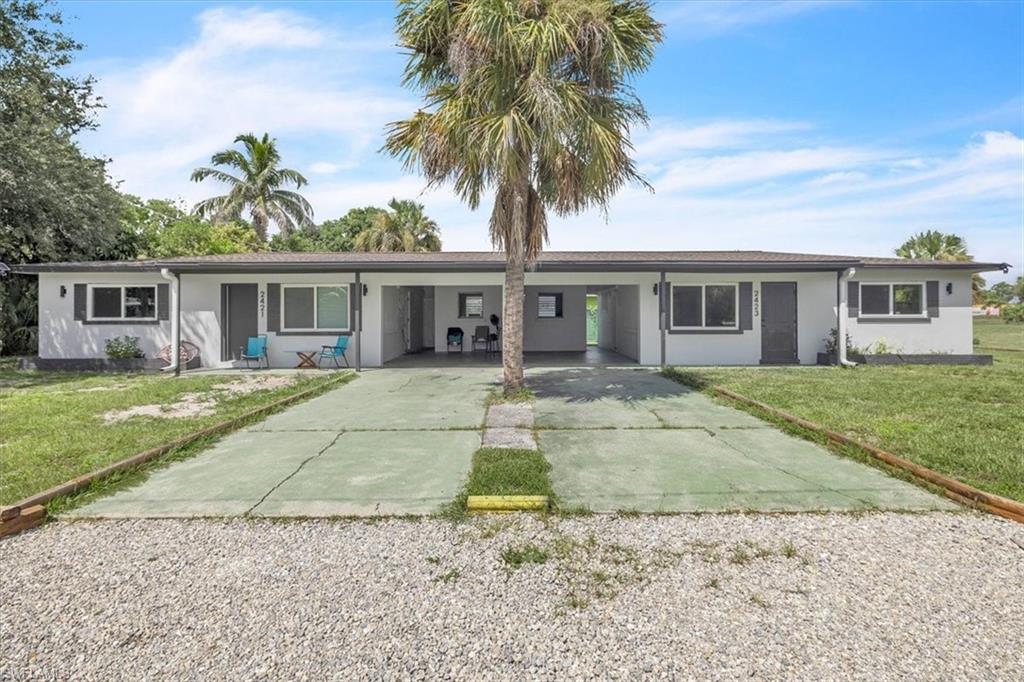 Gray single-story duplex with two entrances, covered porches, and a palm tree in the driveway.