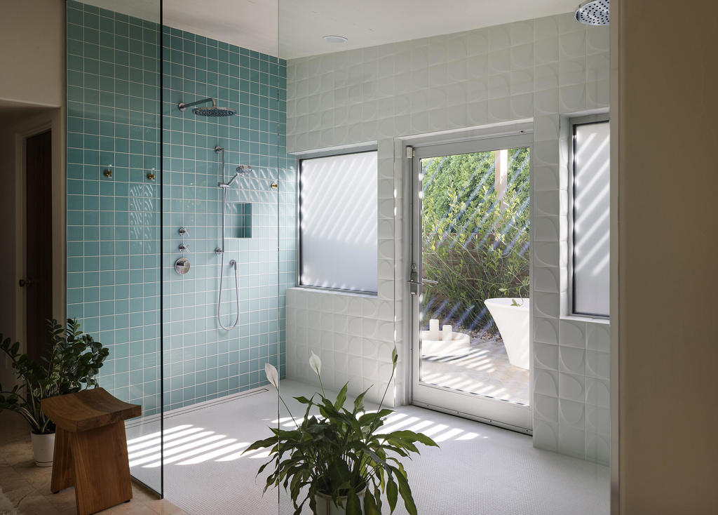 Modern bathroom with a teal-tiled glass shower and a door opening onto a sunny patio.