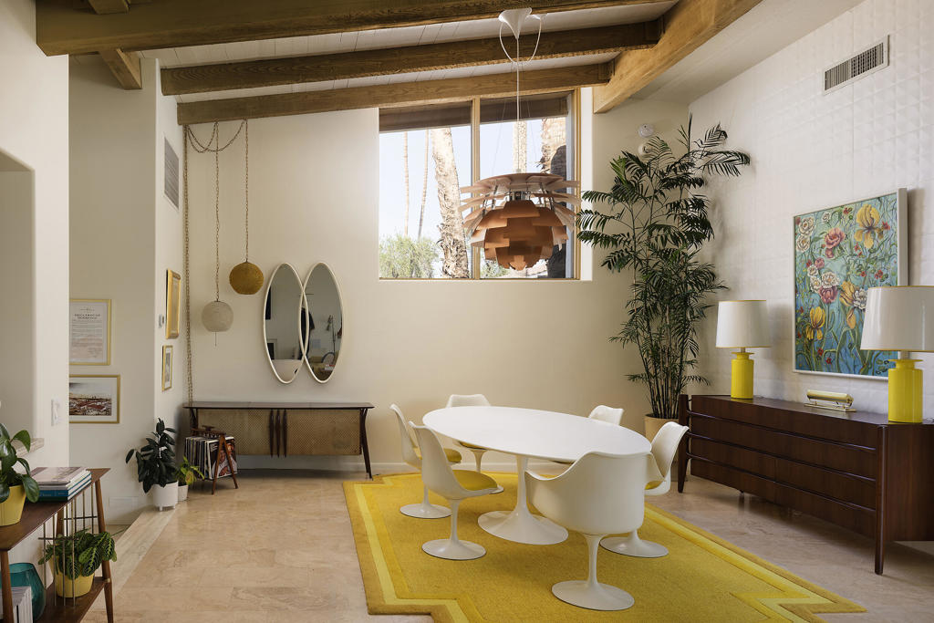 Dining room with exposed wood beams, a white table, and a bright yellow rug.