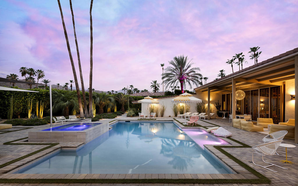 Swimming pool and raised spa beside a covered patio, illuminated under a pink dusk sky.