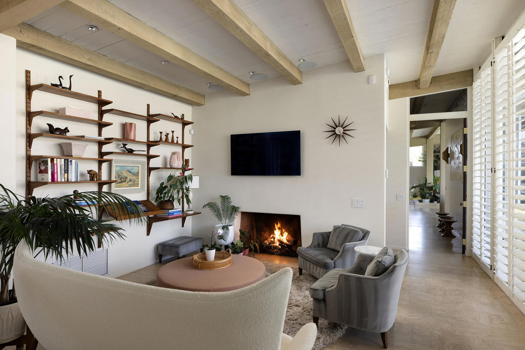Living room with exposed wood beams, built-in shelves, and a lit fireplace.