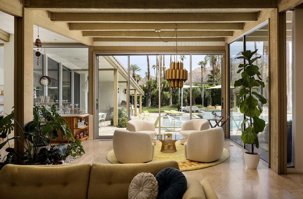 Living room with exposed beams and glass doors overlooking a pool and mountains.