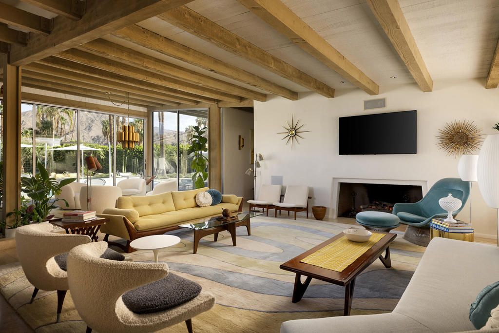 Living room with exposed wood beams, a fireplace, and large garden-facing windows.