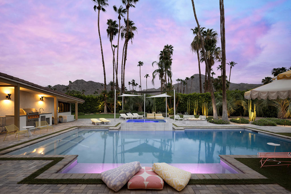 Backyard swimming pool at dusk with palm trees, outdoor lounge seating, and mountains beyond.