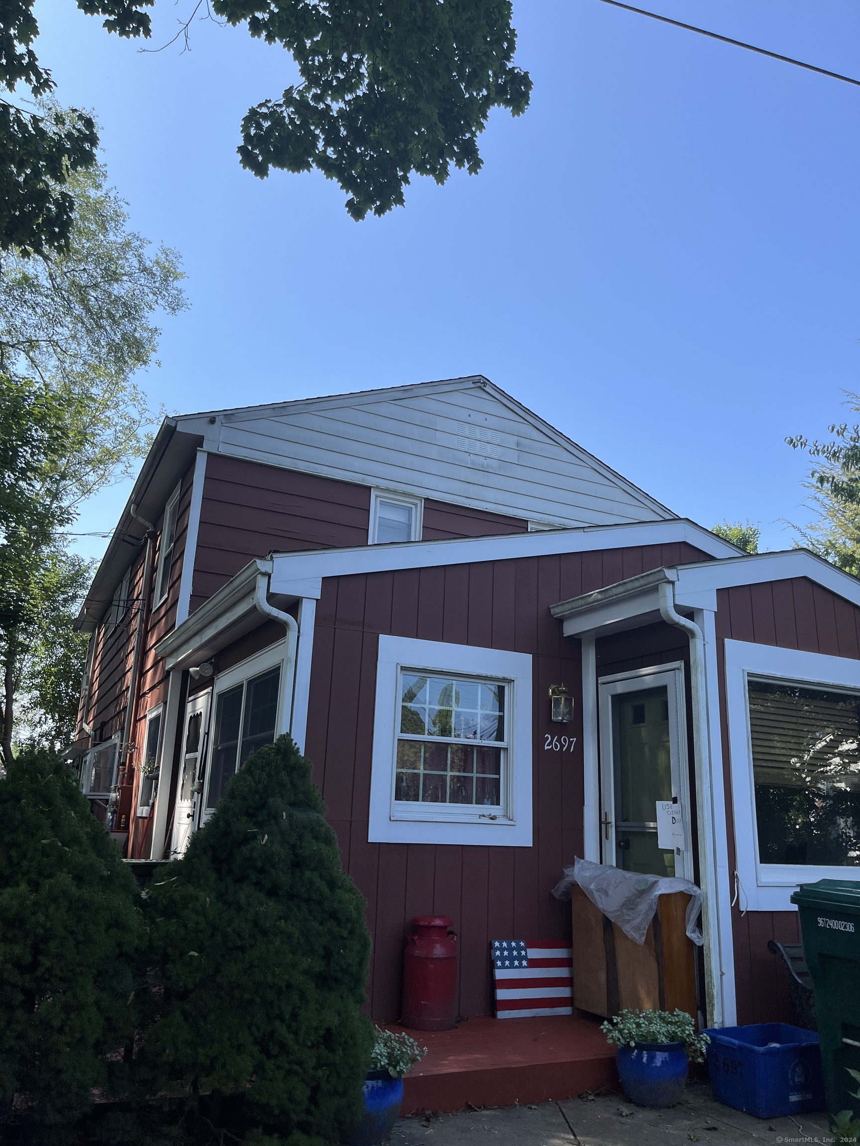 Red-sided two-story house with white trim, a small porch, and the number 2697 beside the entrance.
