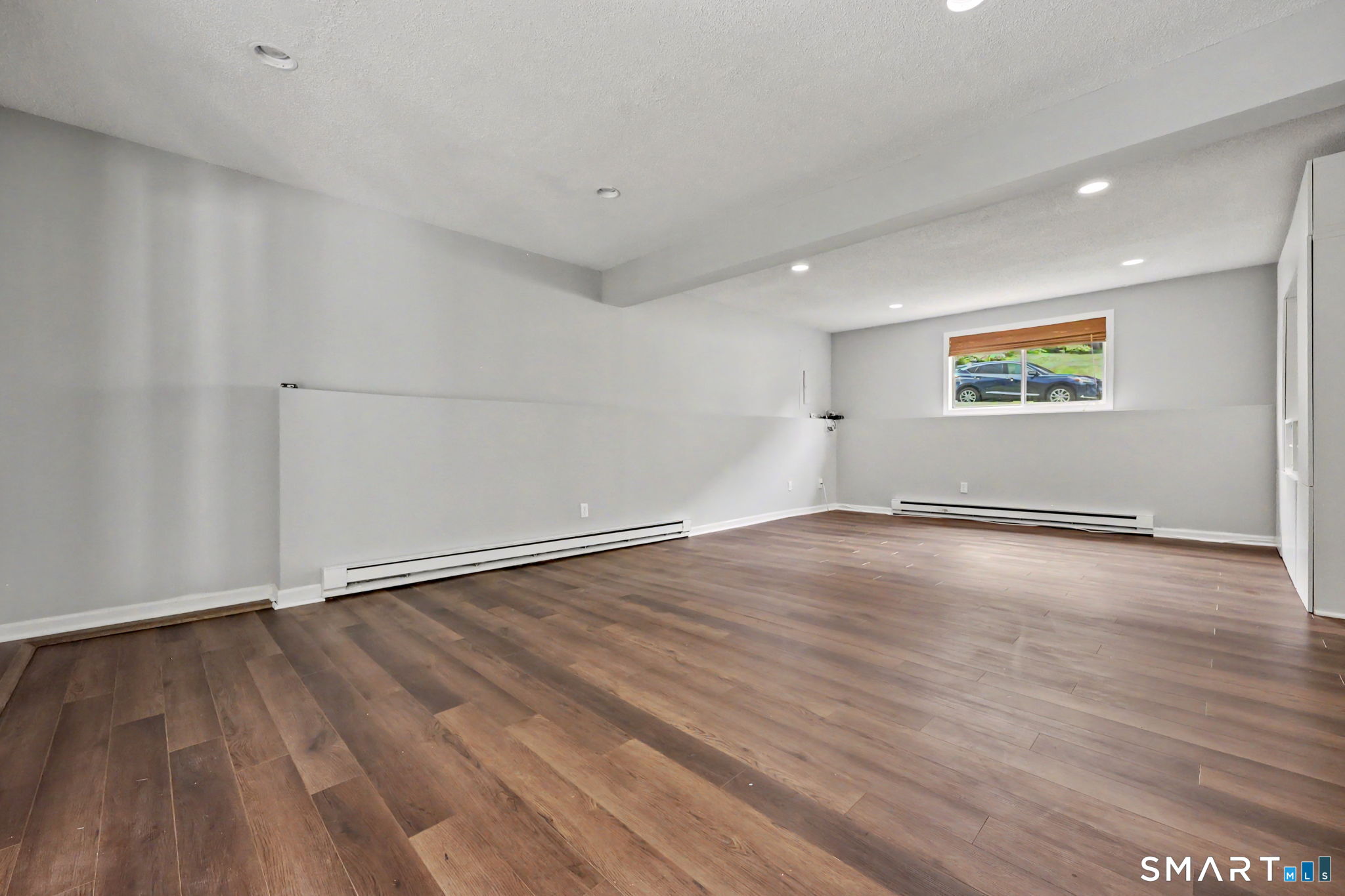 Empty finished room with dark plank flooring, gray walls, and a small window.