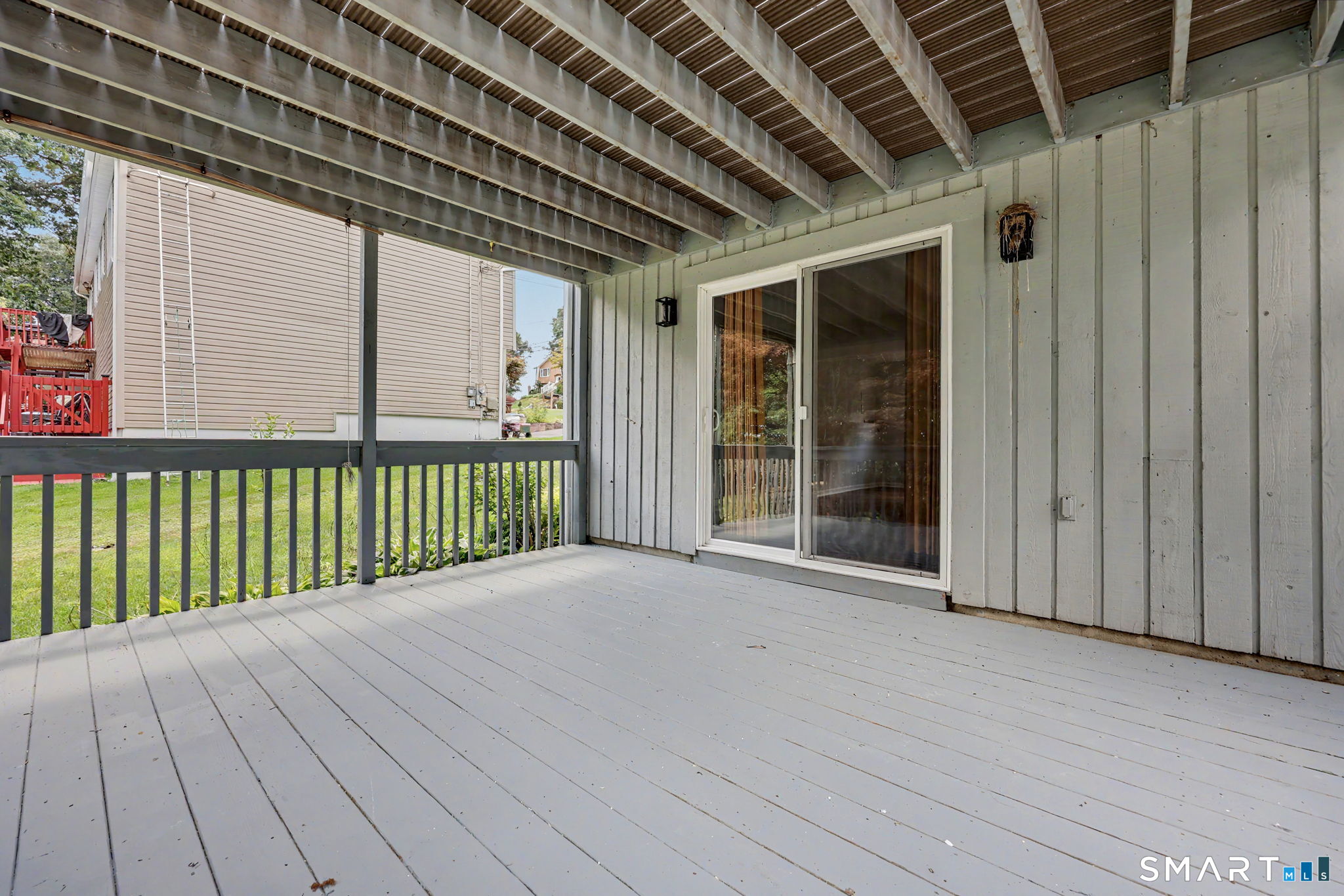 Covered gray deck with exposed roof beams, a railing, and sliding glass doors.