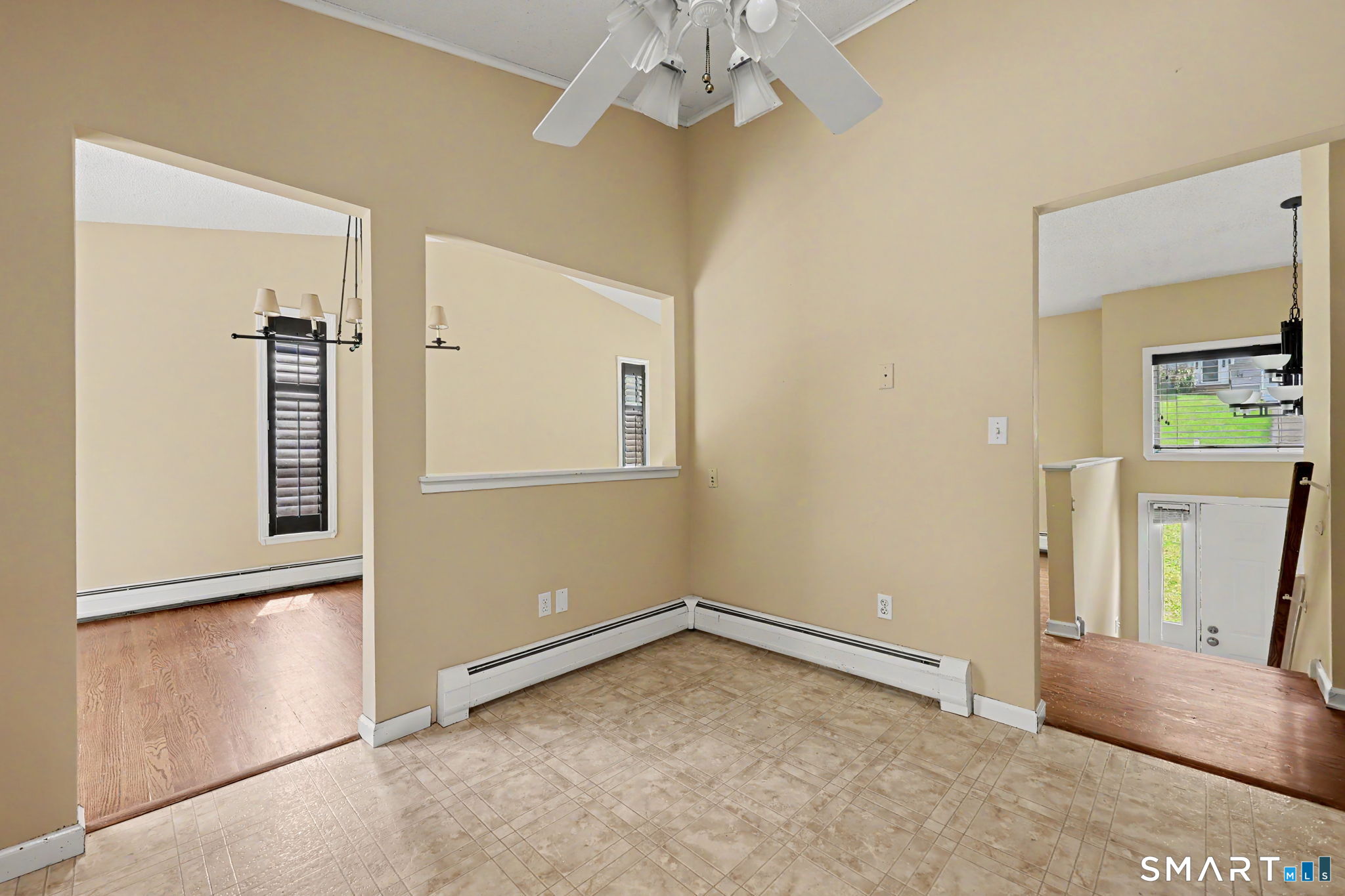 Empty beige room with tiled flooring, a ceiling fan, and openings to adjoining hardwood-floored rooms.