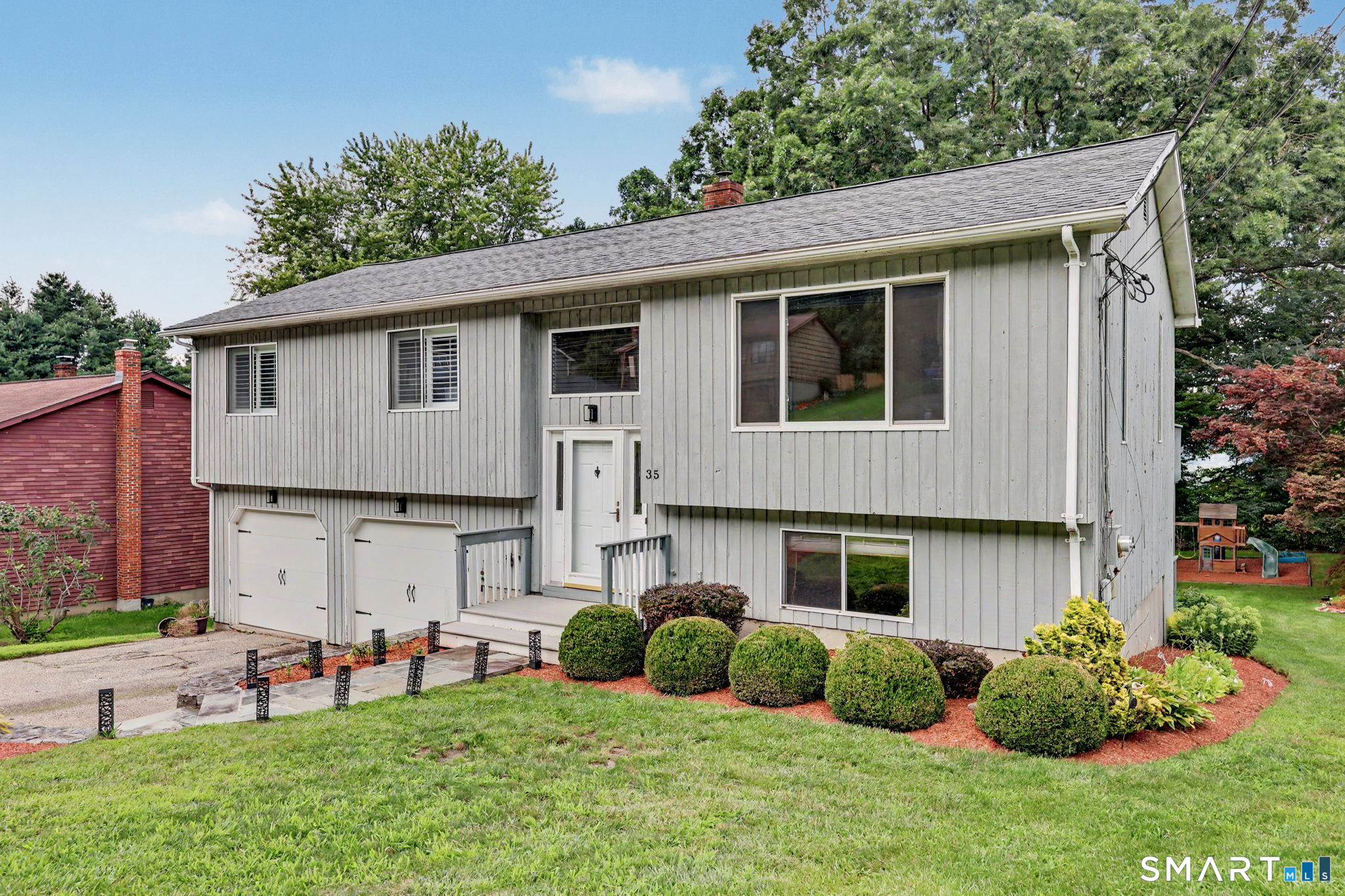 Gray split-level home with two garage doors, a landscaped lawn, and rounded shrubs along the front.