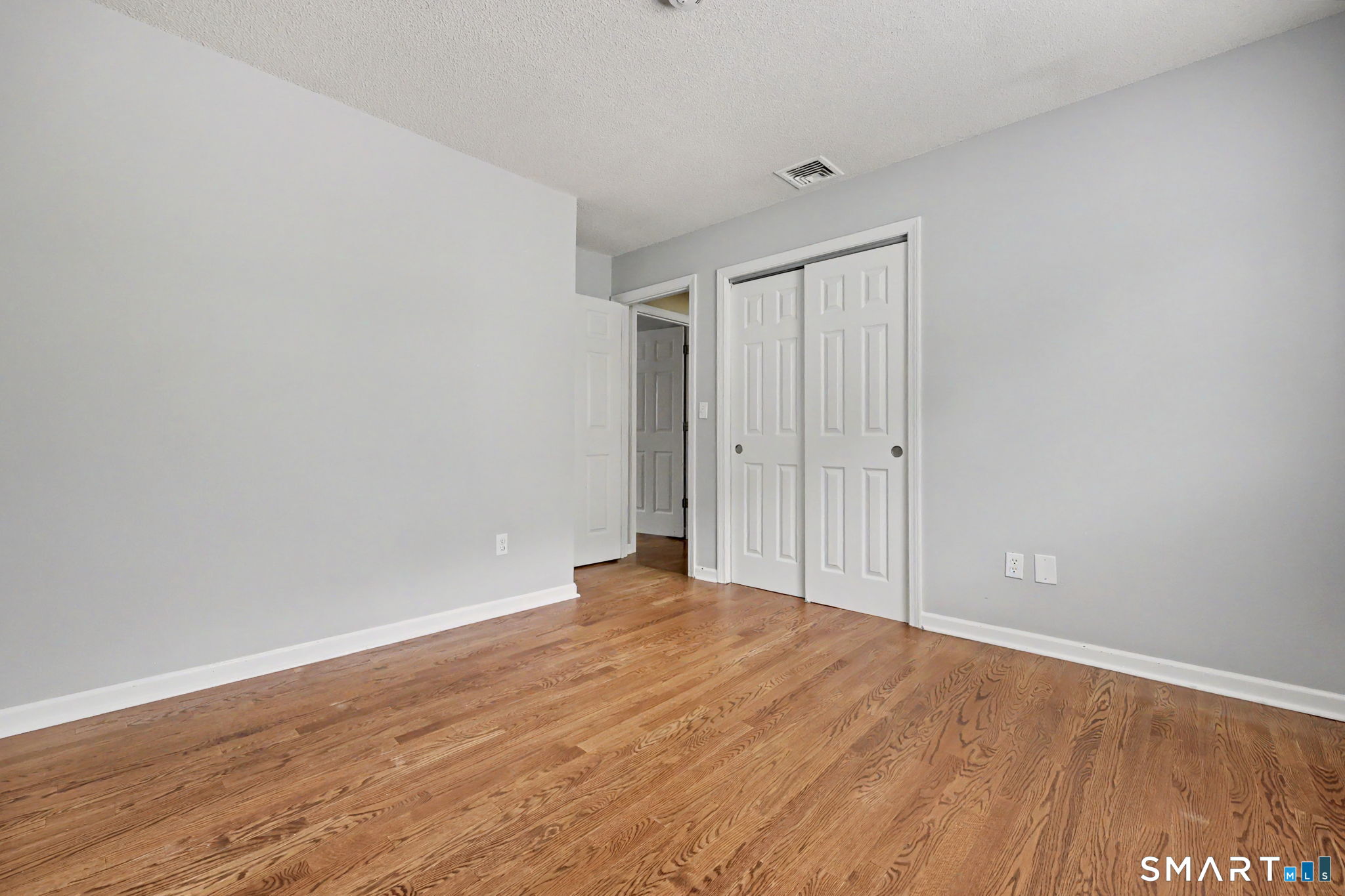 Empty bedroom with hardwood floors, gray walls, and white closet doors.