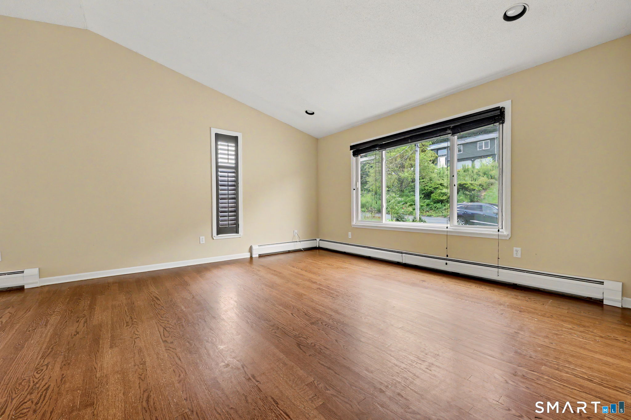 Vacant room with hardwood floors, beige walls, and a large window with blinds.