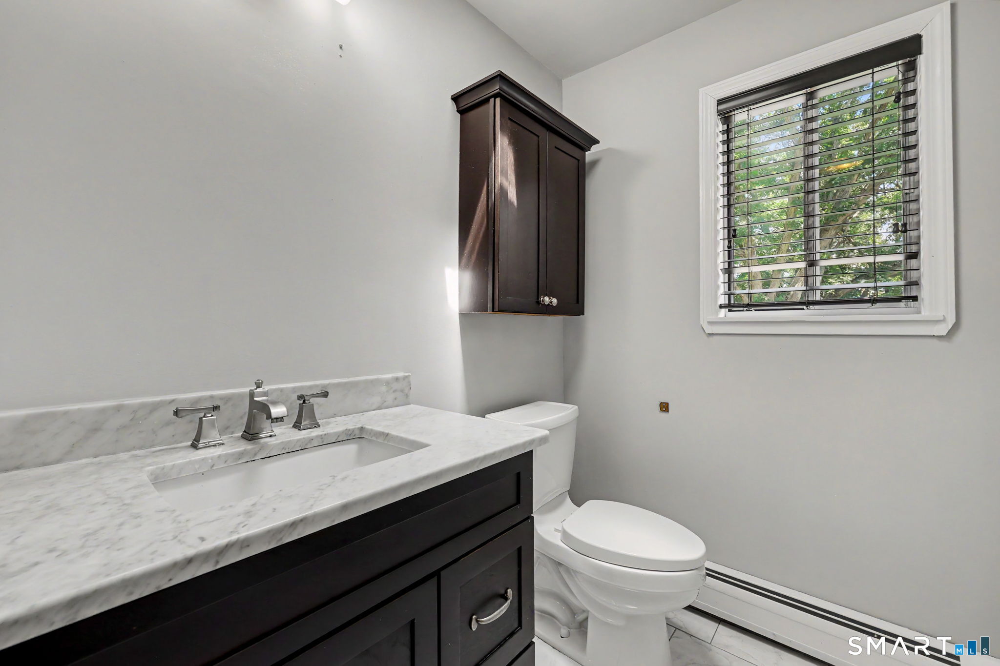 Bathroom with a marble vanity, dark cabinetry, and a window with black blinds.