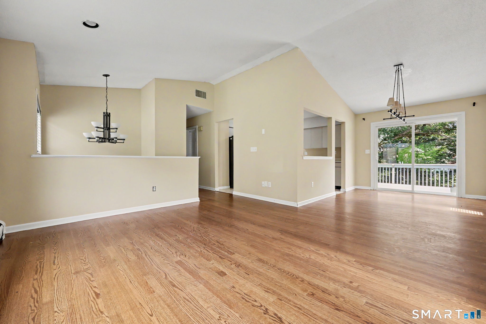 Vacant open-plan living and dining area with wood floors and sliding doors to a deck.