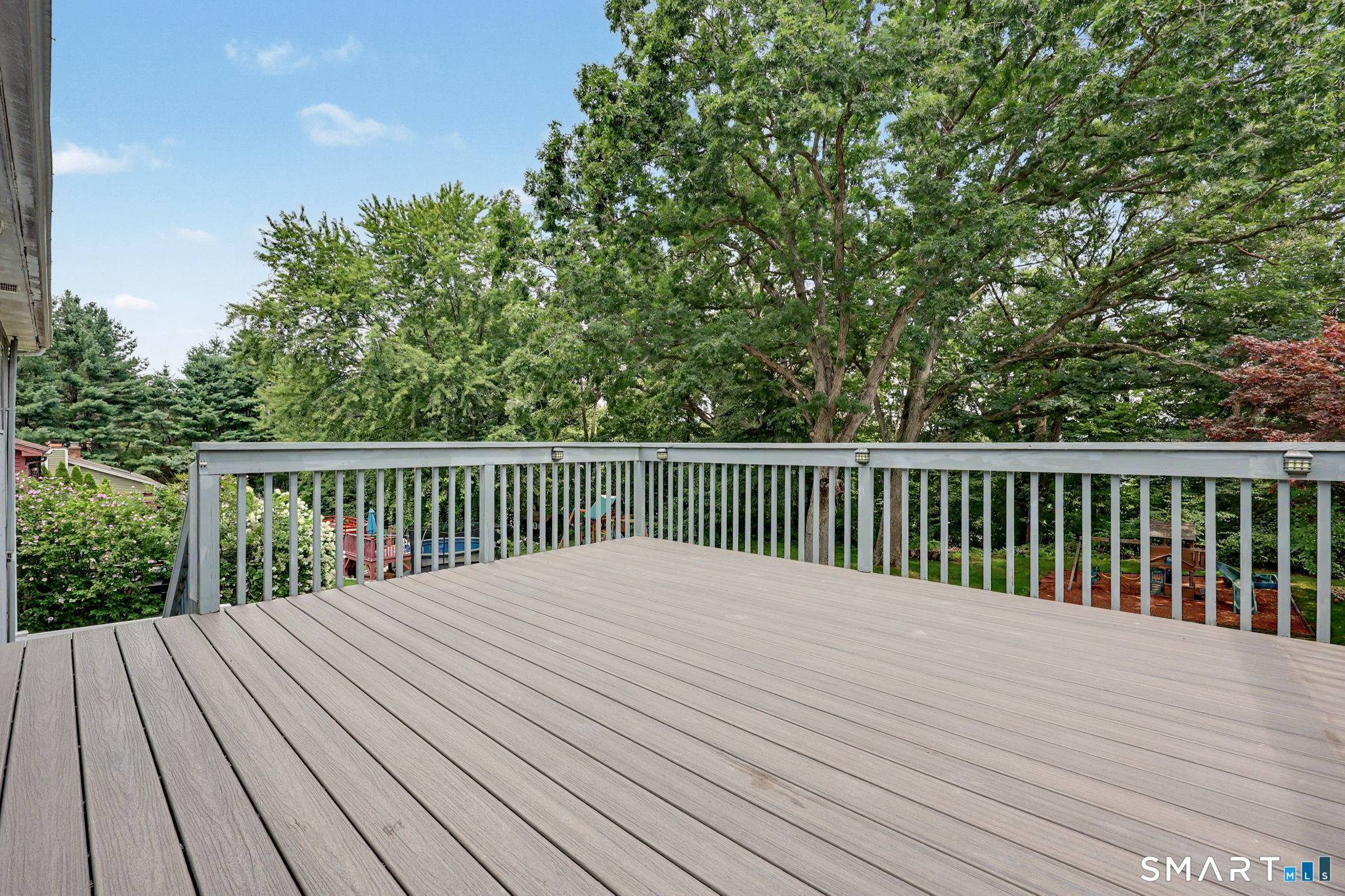 Gray composite deck overlooking a leafy backyard beneath mature trees.