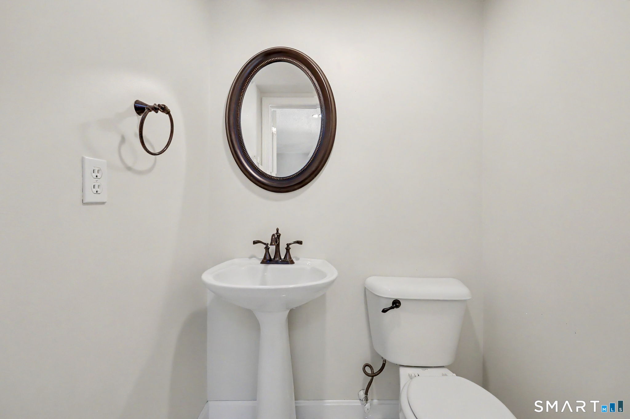Small bathroom with a pedestal sink, toilet, and oval mirror above the sink.