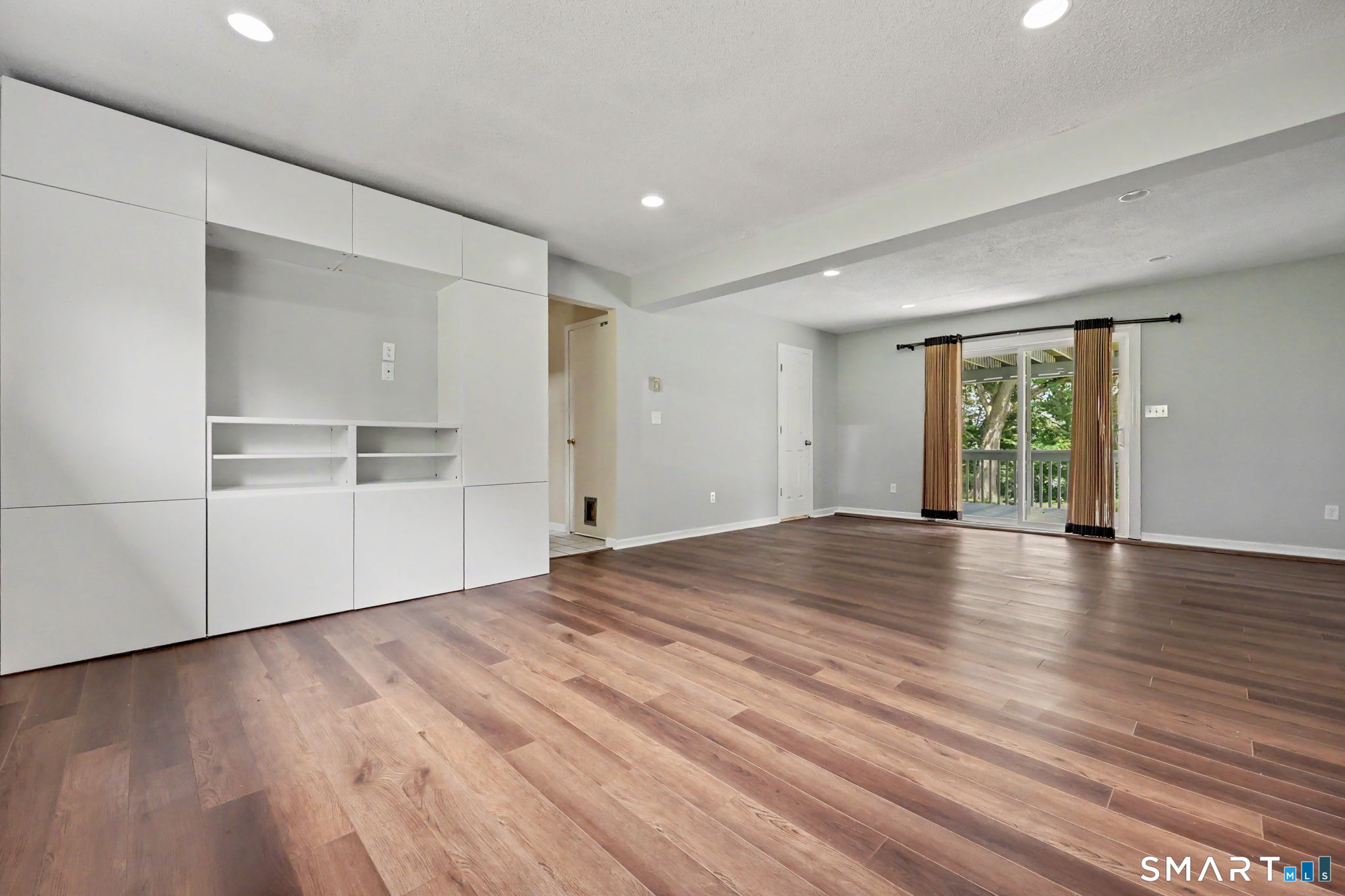 Vacant living room with built-in white cabinets, wood-look flooring, and sliding doors to a deck.