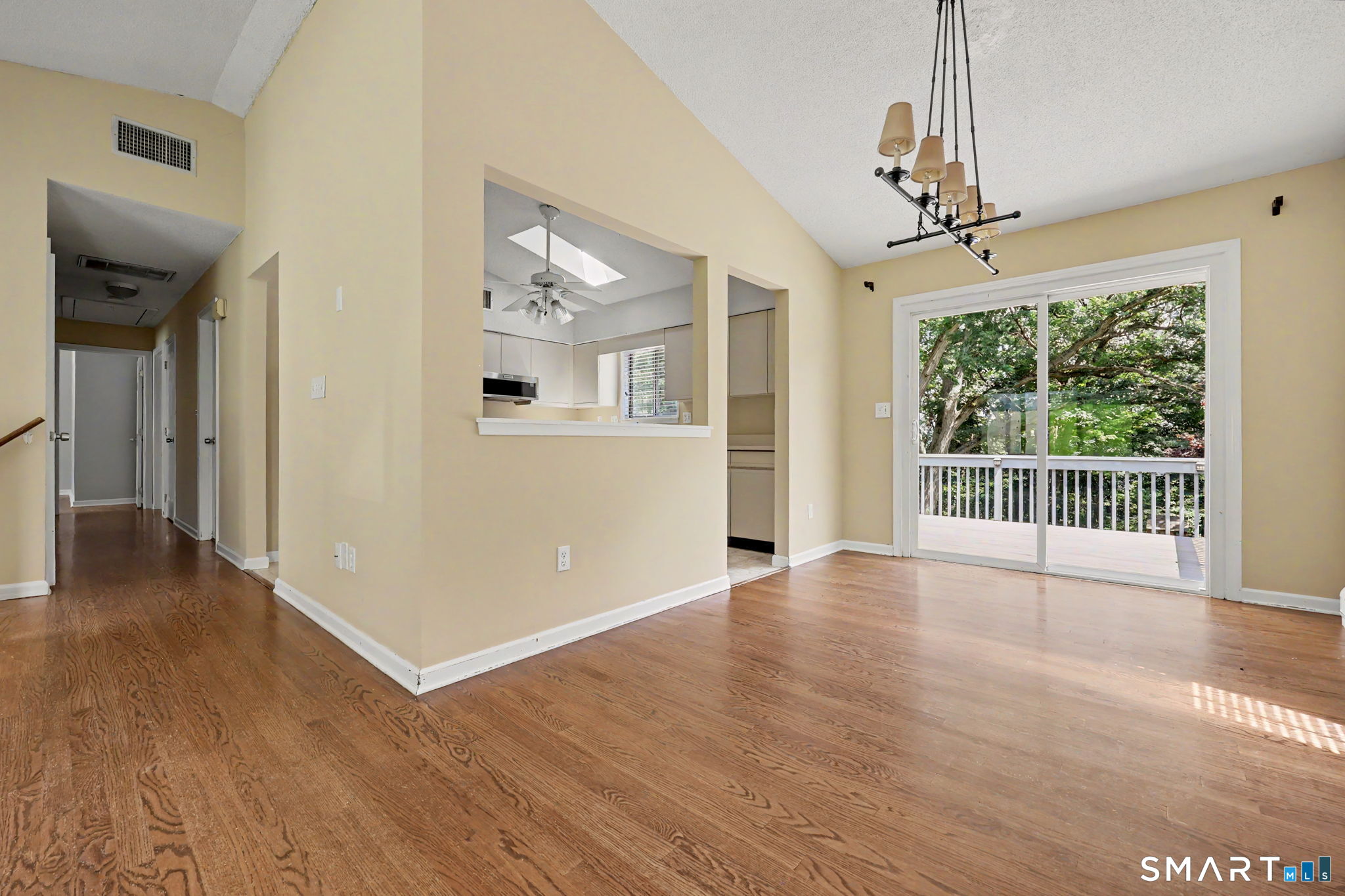 Unfurnished dining area with hardwood floors, a chandelier, and sliding doors to a tree-lined deck.