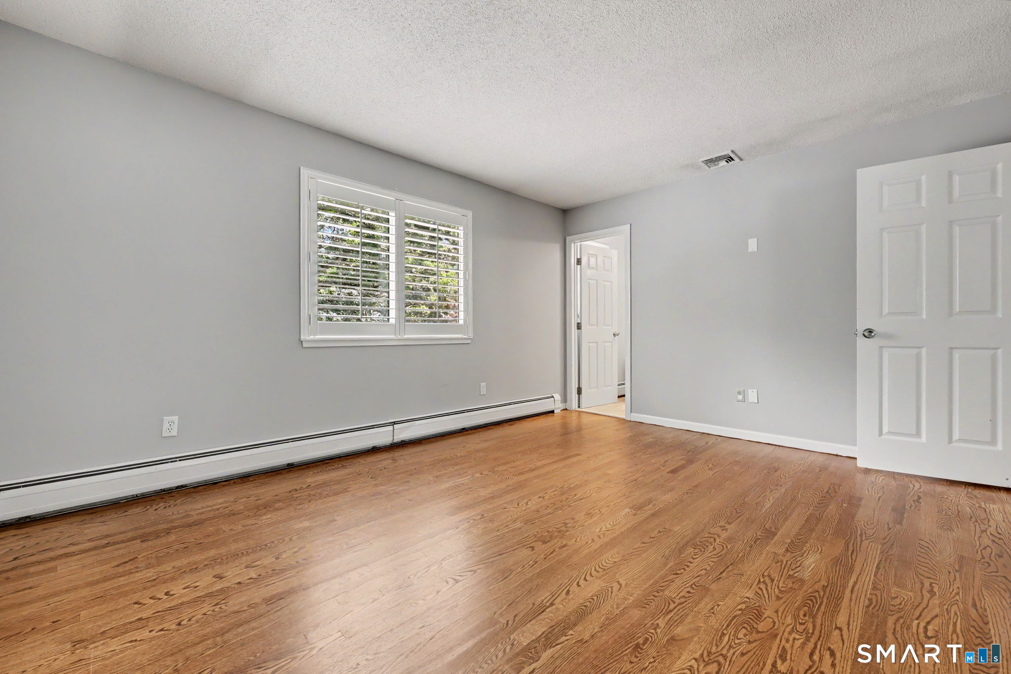 Empty room with hardwood floors, gray walls, and a shuttered window.