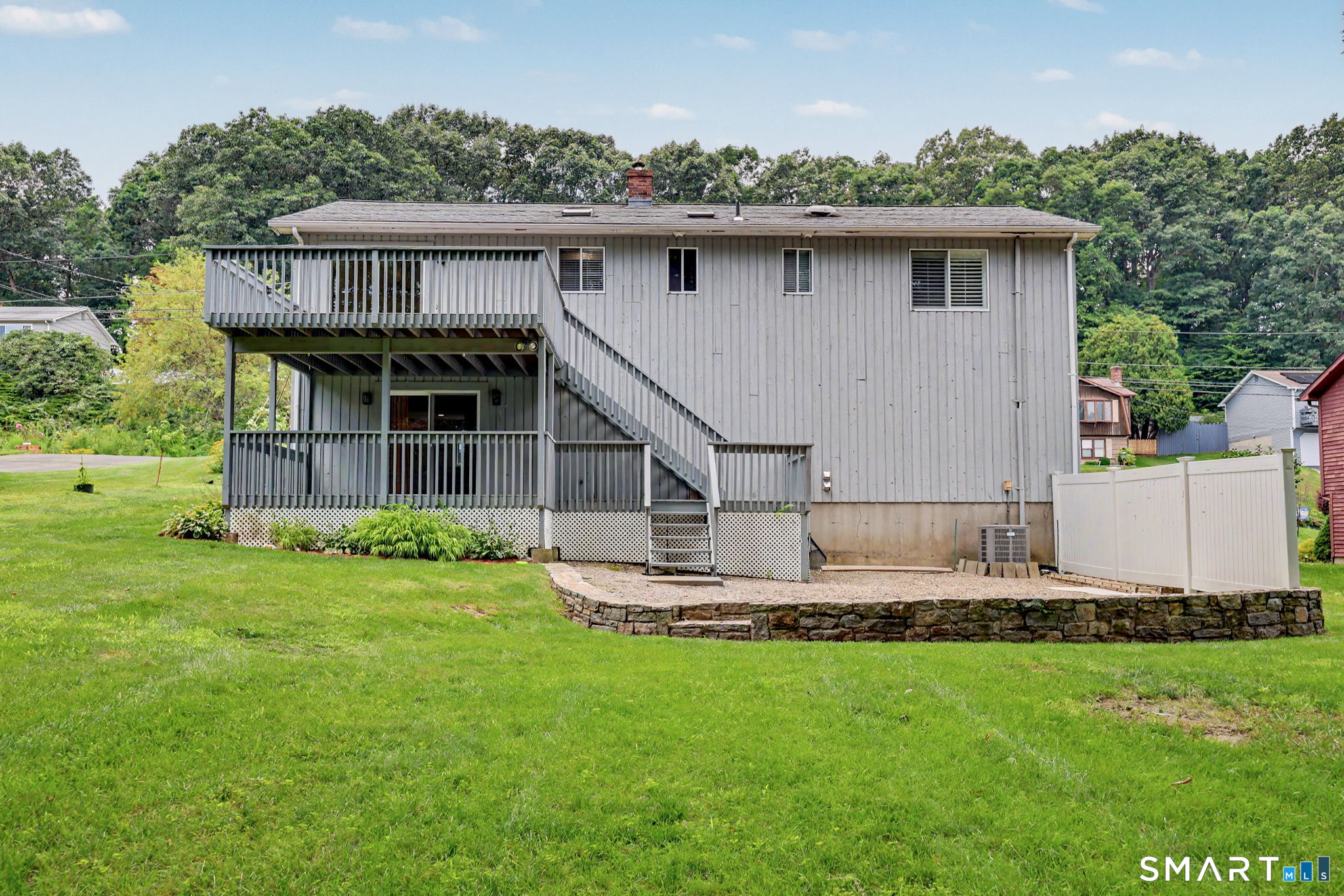 Rear of a gray two-story house with an elevated deck, exterior stairs, and a broad lawn.