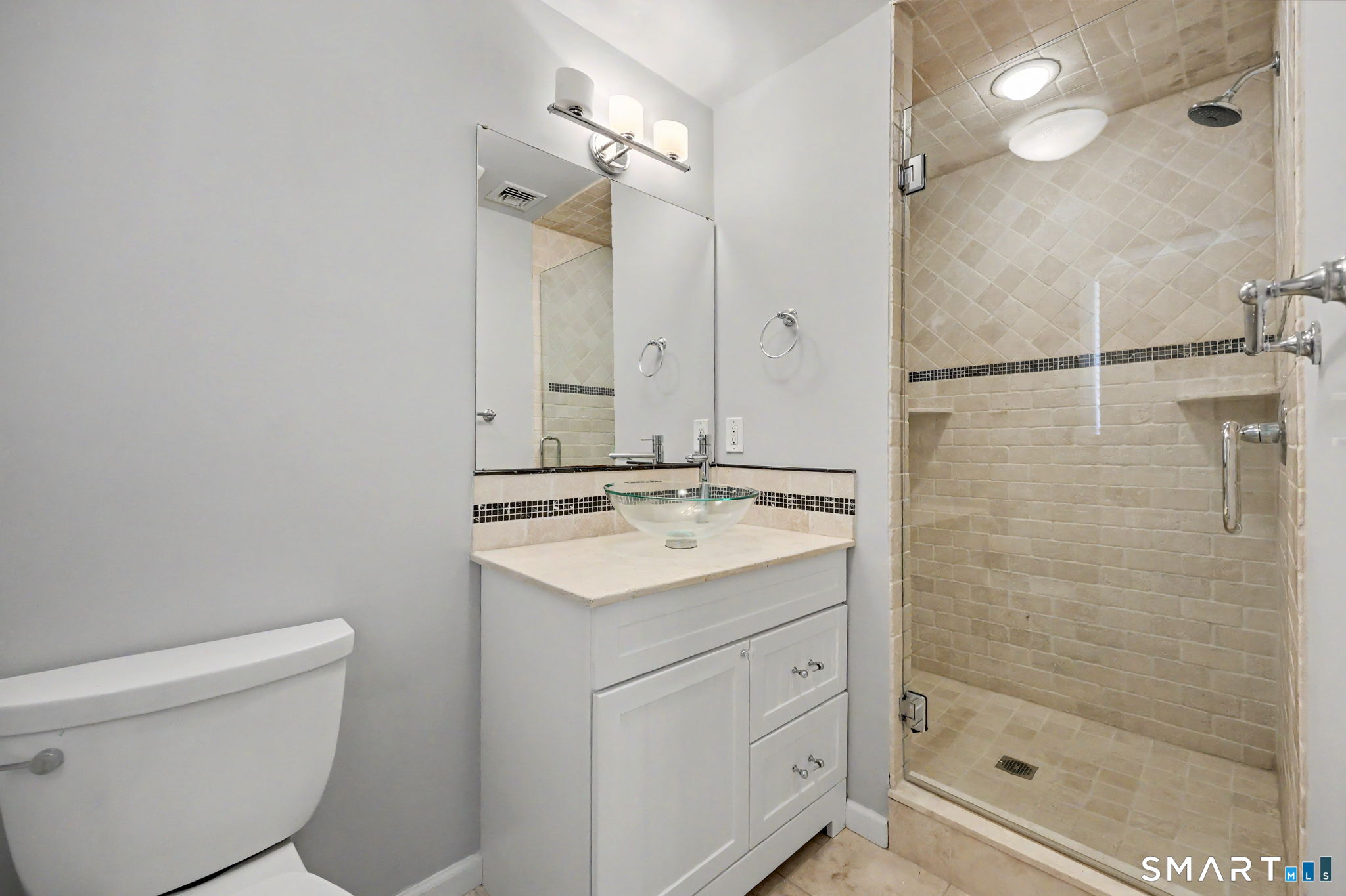 Bathroom with a glass vessel sink vanity and beige tiled walk-in shower.
