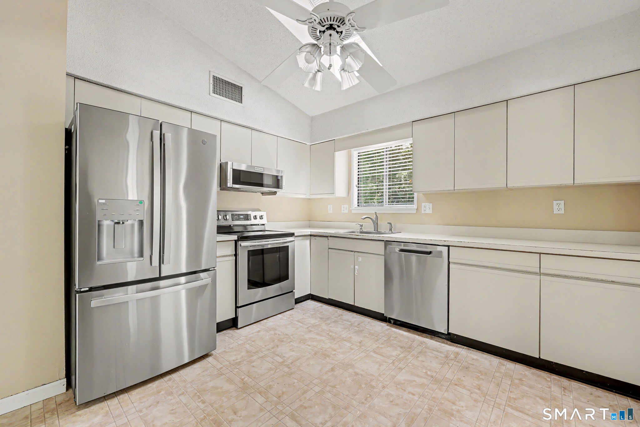 Kitchen with white cabinets, stainless steel appliances, beige tile floor, and a ceiling fan.