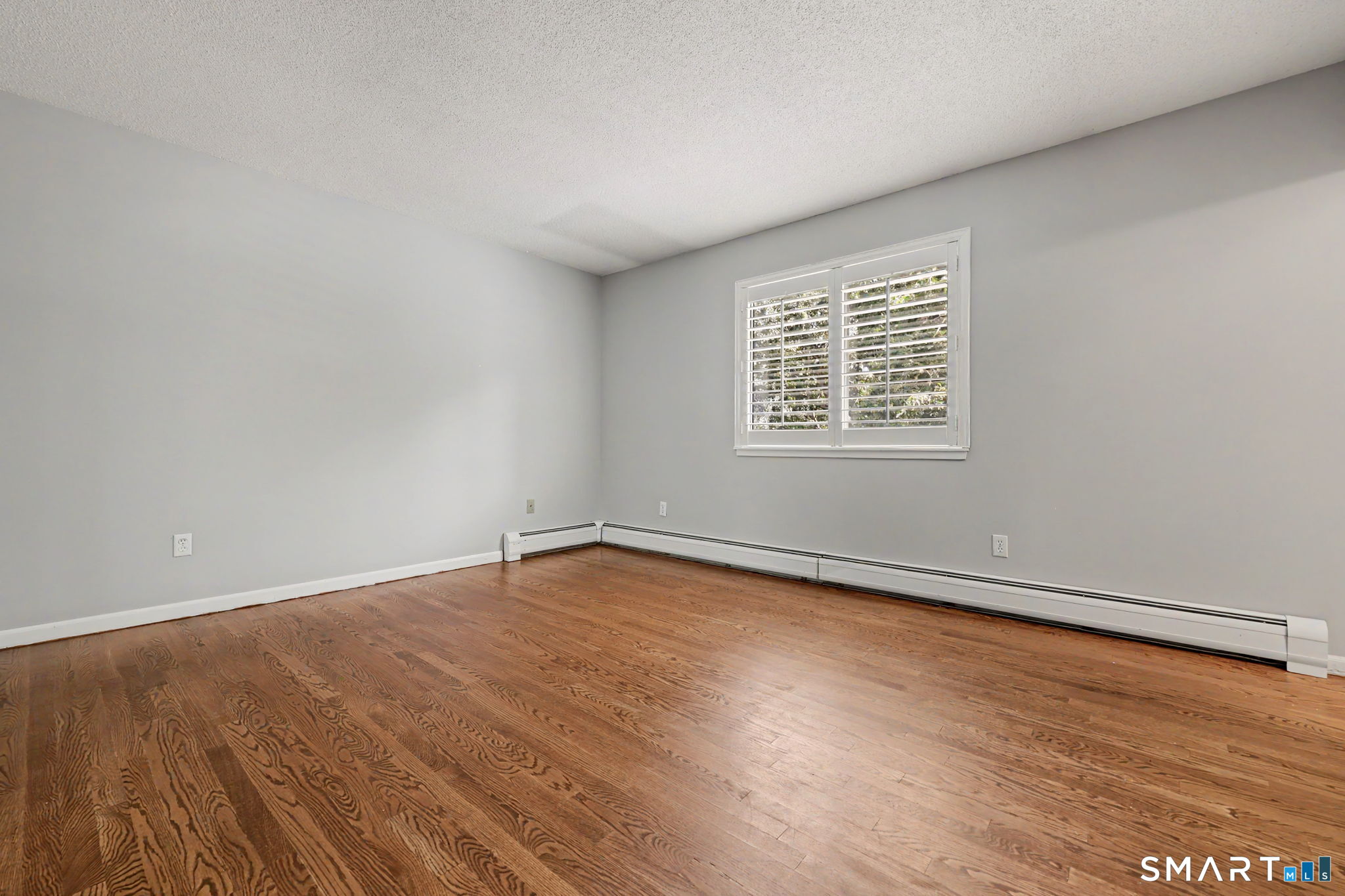 Empty room with hardwood floors, gray walls, and a shuttered window.
