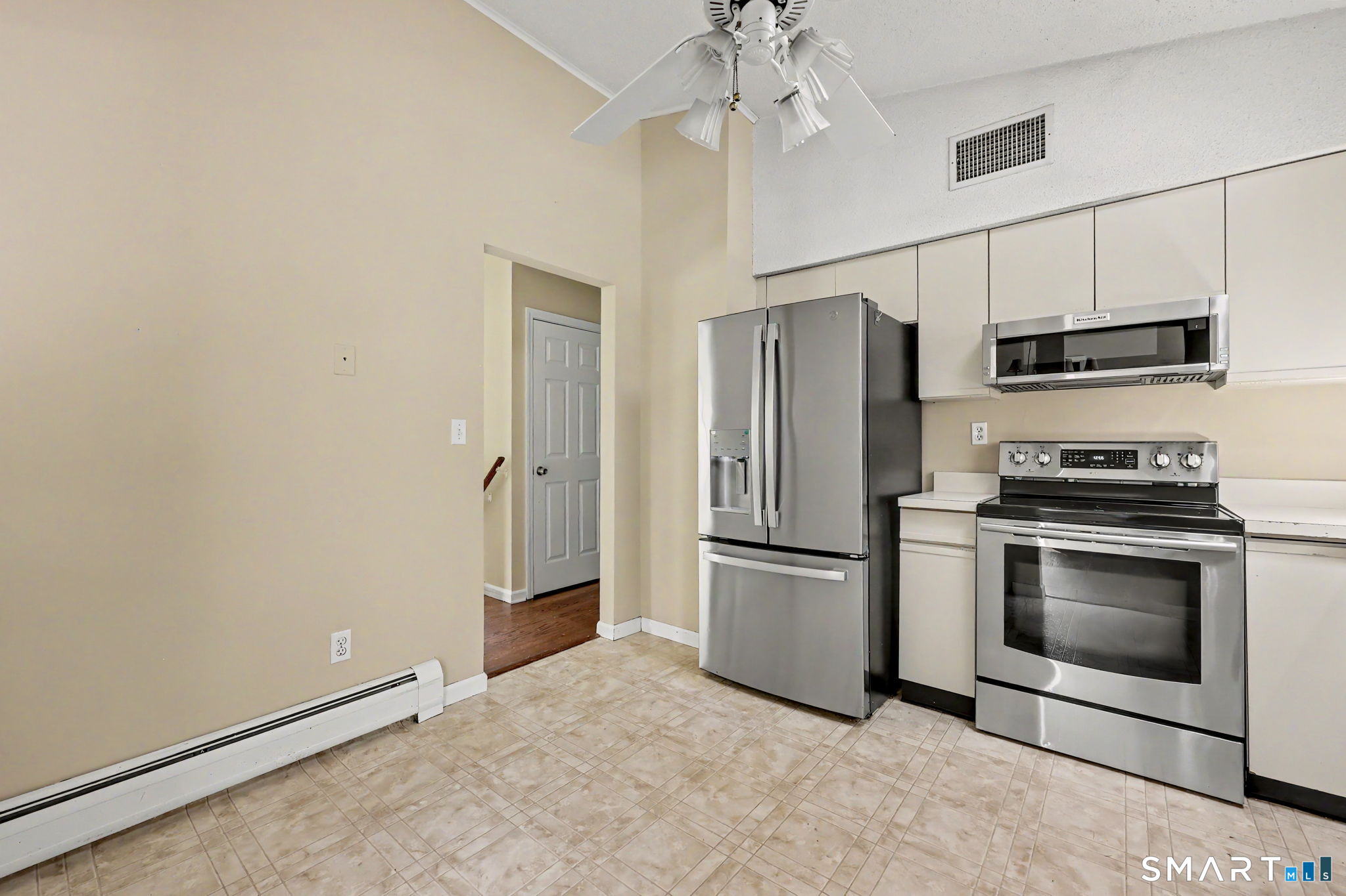 Kitchen with white cabinets, stainless steel appliances, beige tile flooring, and a ceiling fan.
