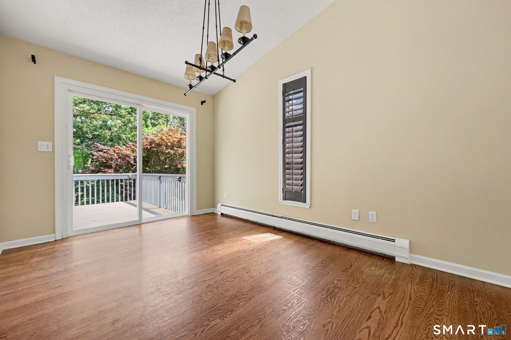 Empty dining room with hardwood floors, chandelier, and sliding glass door to a tree-lined deck.