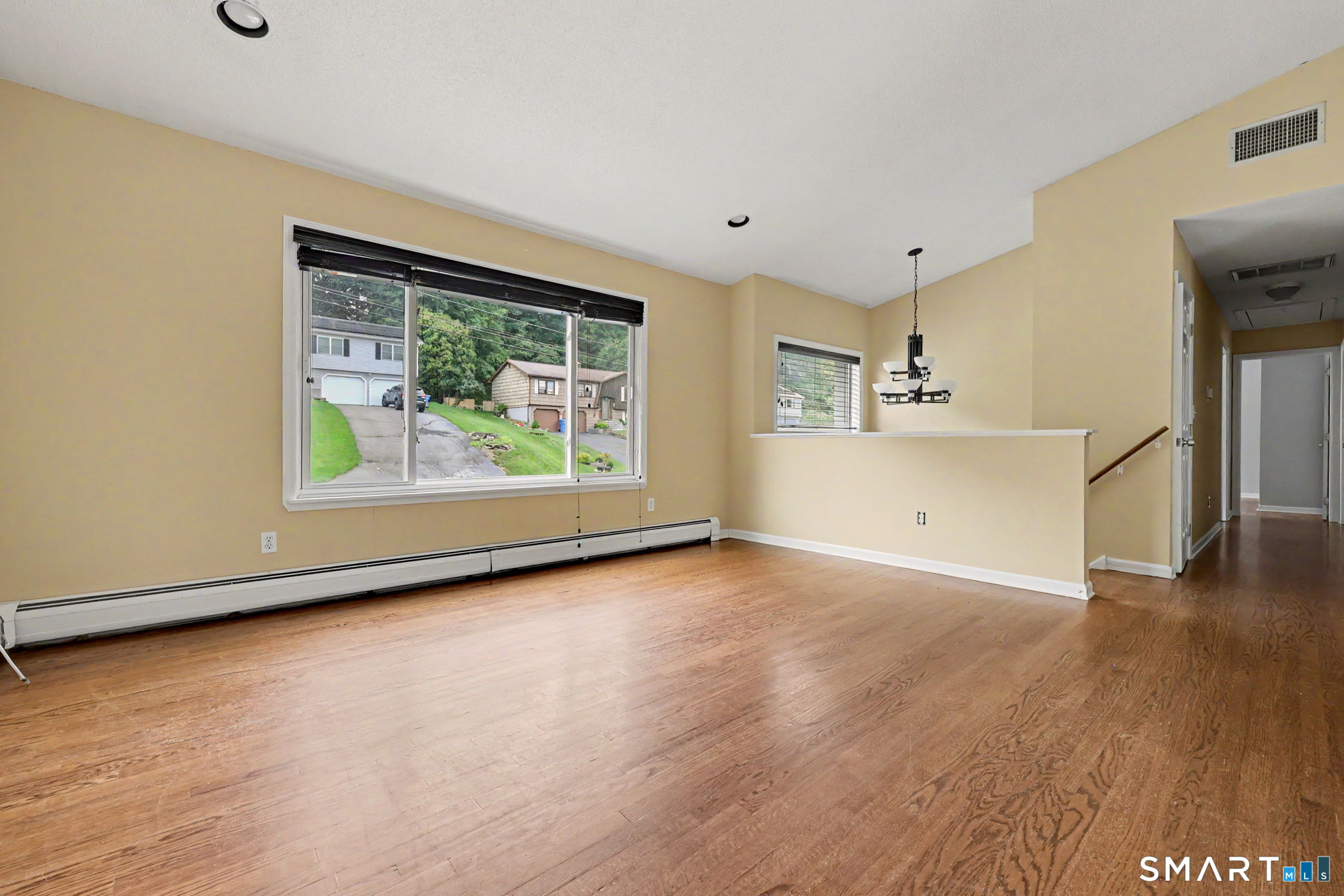 Empty dining area with hardwood floors, a large window, and a chandelier.